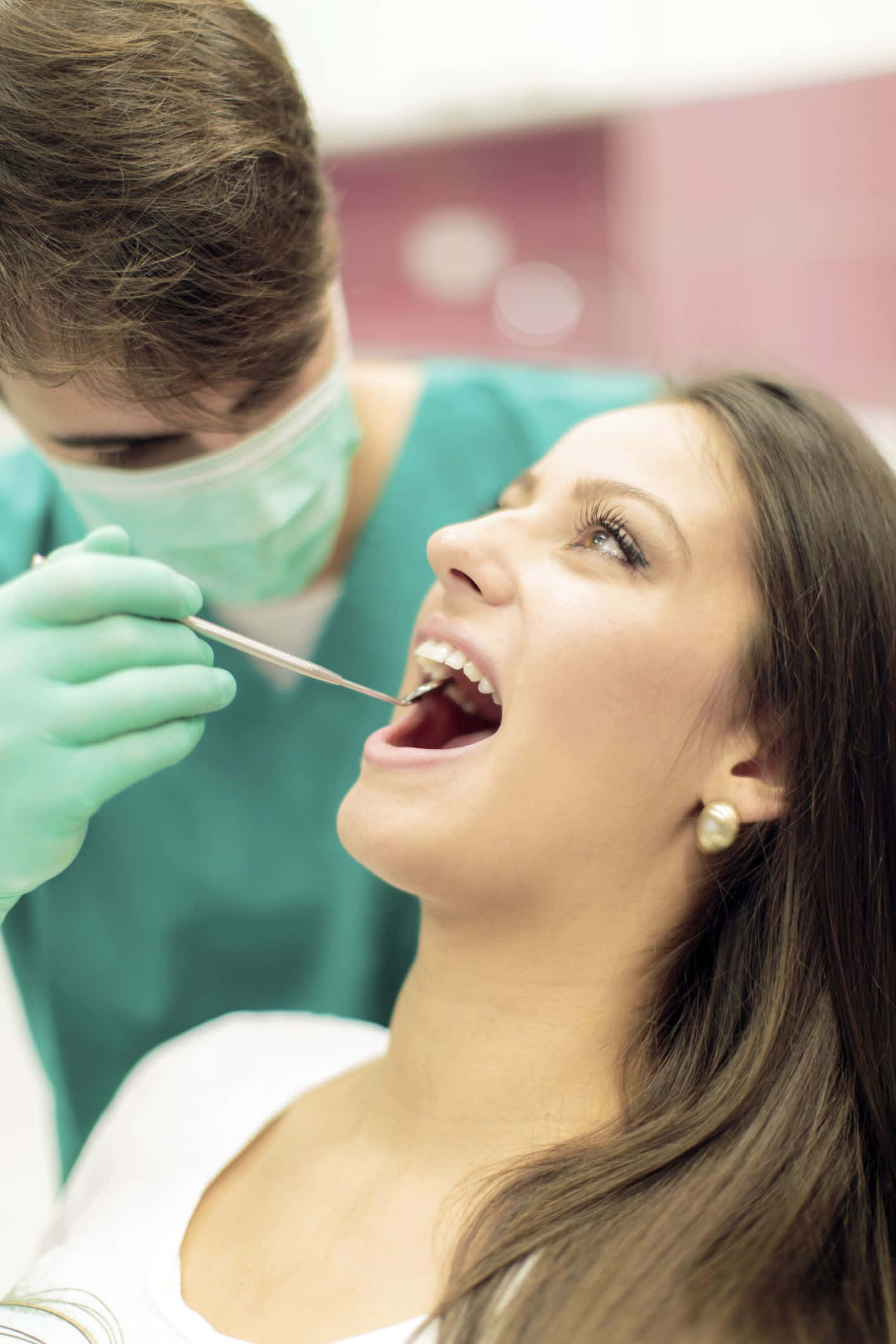 Dentist 桌布 壁紙 — 一名女士躺在牙科椅上，戴著口罩的牙醫用工具檢查她的牙齒。