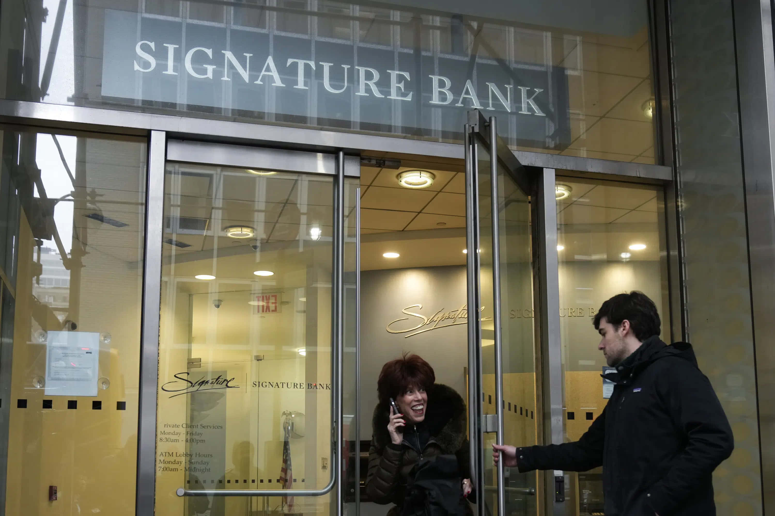 Bank 桌布 壁紙 — 一名女子一邊笑著講電話，一邊走出現代玻璃幕牆的Signature Bank分行，一名男子為她扶著門。