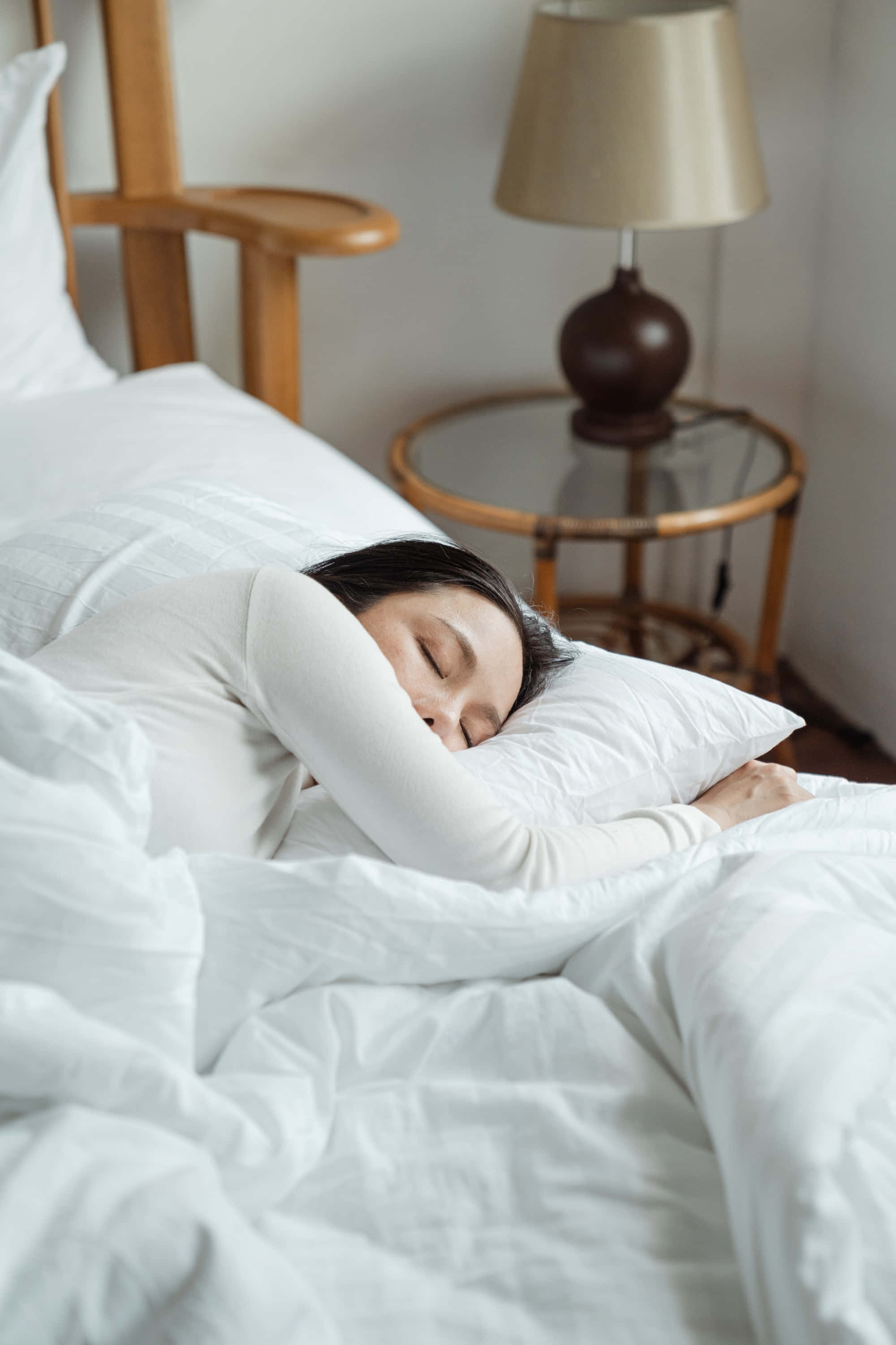 Sleep 桌布 壁紙 — 一名女子在柔和光線的睡房中，裹著白色床單，在帶有燈的木製床頭几旁安詳地入睡。