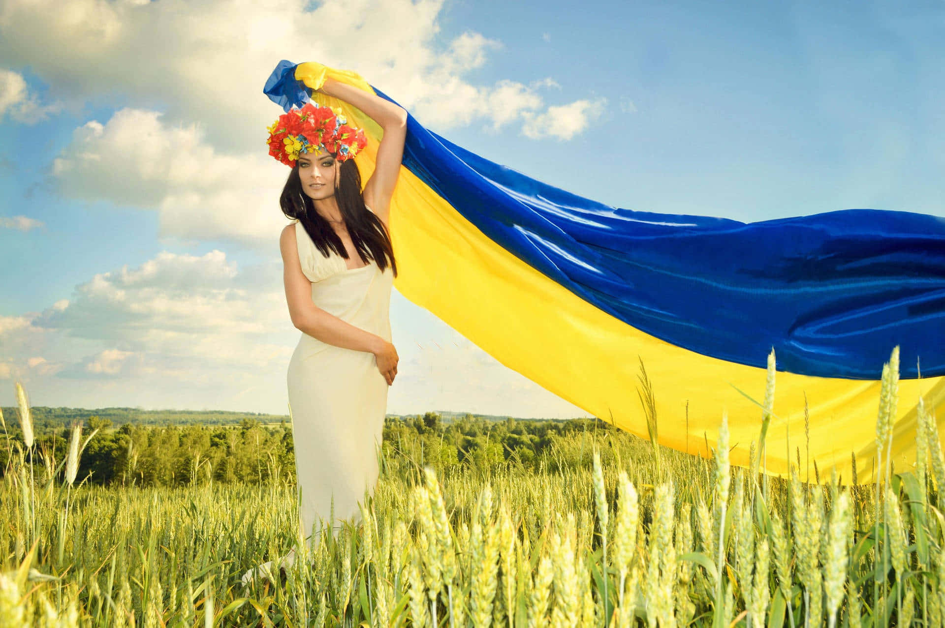 Caption: Pride in Roots - Ukrainian Girl Waving Flag 壁紙 — 一名女子在麥田裏，在藍天白雲下高舉烏克蘭國旗。