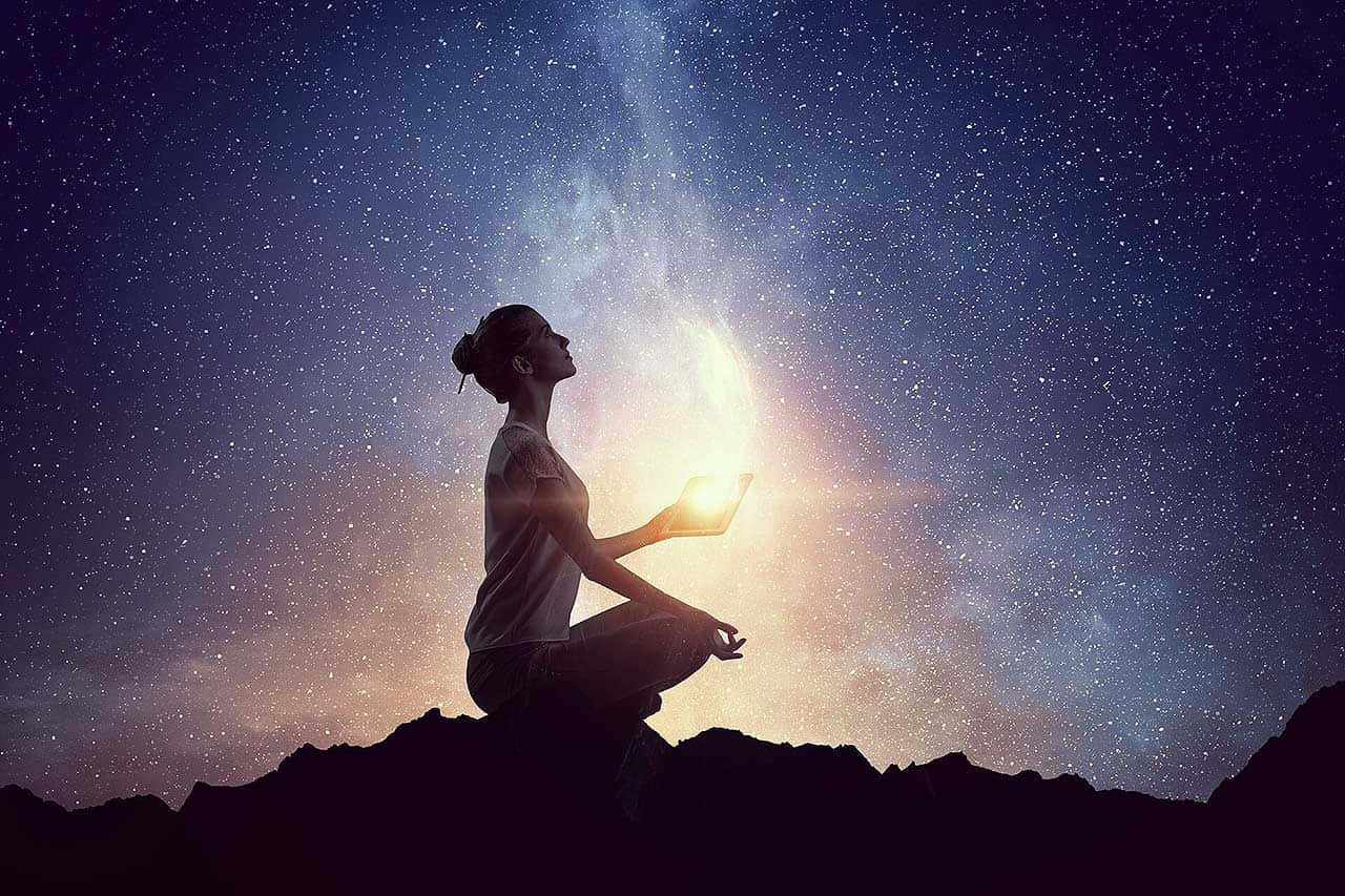 靈魂 桌布 壁紙 — 一名女性在山頂上冥想，頭上是繁星點點的夜空，上方有一道發光的天體光芒。