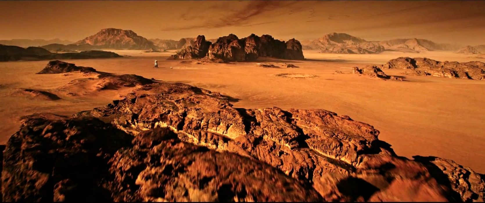 Mars Landscape 桌布 壁紙 — 一名孤獨的太空人站在廣闊生鏽的火星平原上，周圍是參差不齊的岩石結構，天空是朦朧的橙色。
