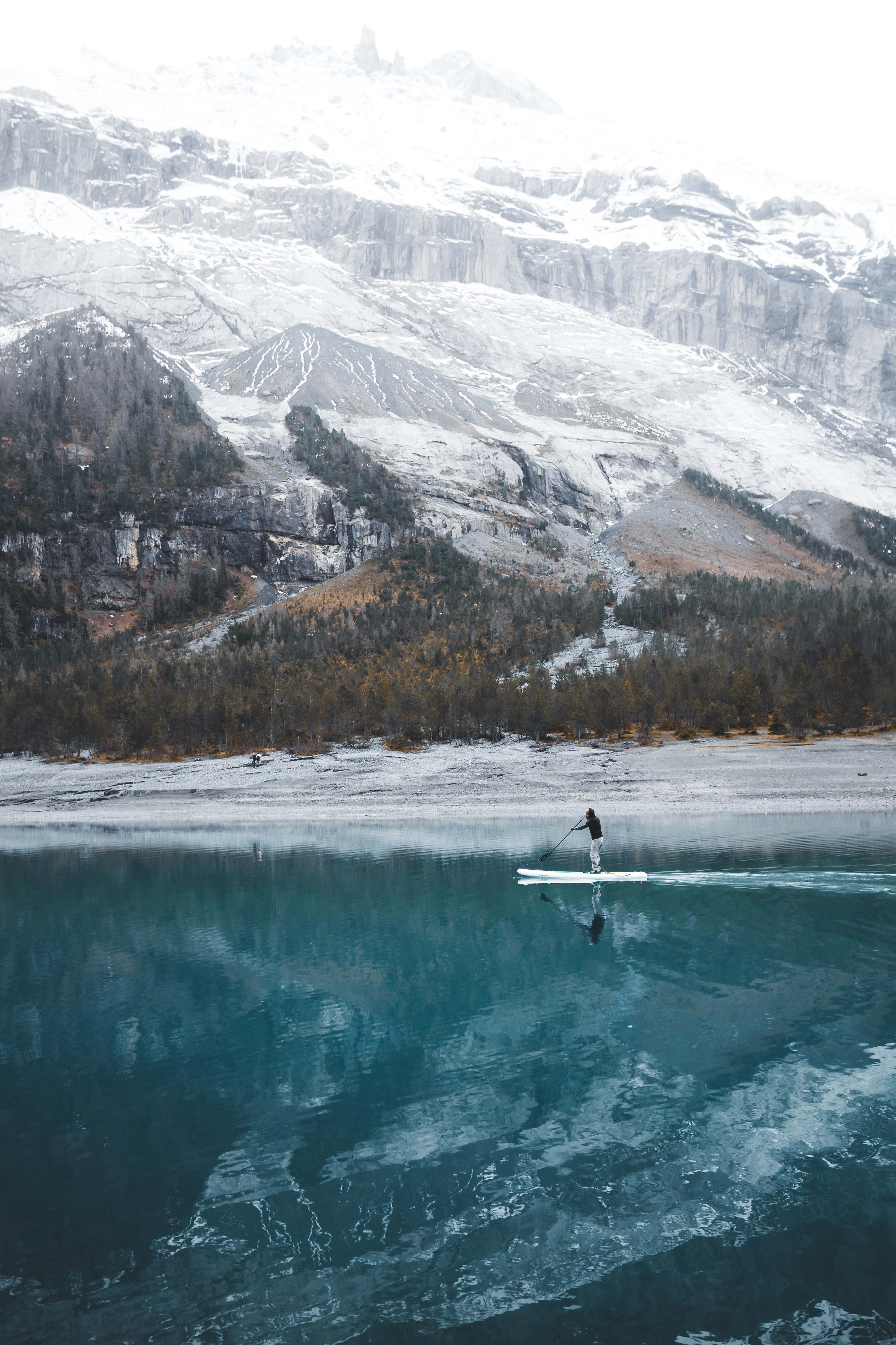 Paddleboarding 桌布 壁紙 — 一名孤獨的槳板划手在如鏡般的碧綠湖面上滑行，四周是高聳的雪山。