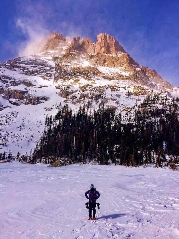Winter Hiking 桌布 壁紙 — 一名孤獨的滑雪者站在白雪覆蓋的高聳山峰前，在清澈的藍天下充滿敬畏。