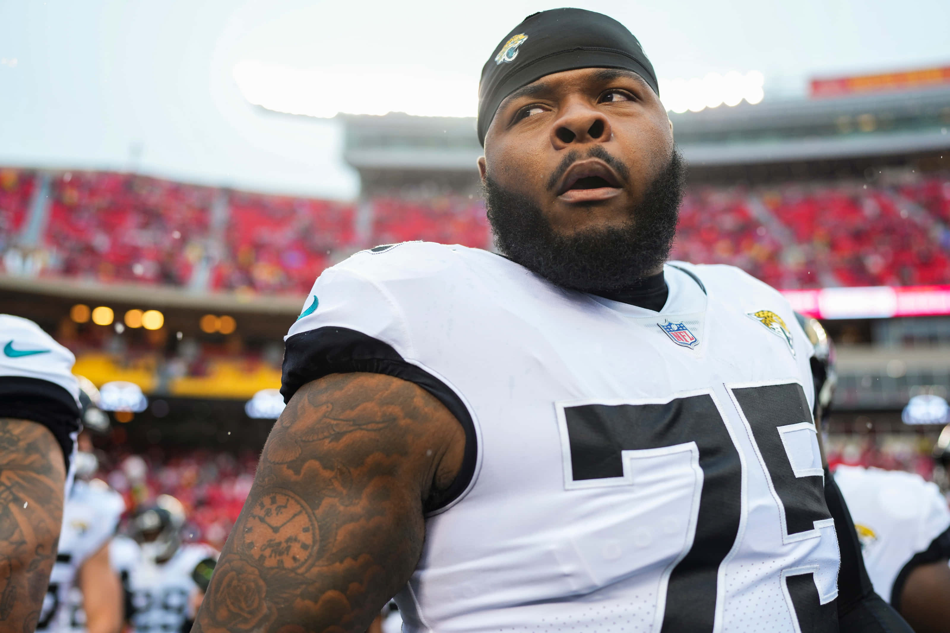 Jawaan Taylor 桌布 壁紙 — 一名專注的NFL球員身穿白色球衣，號碼75，站在球場上，身後是體育場的人群。