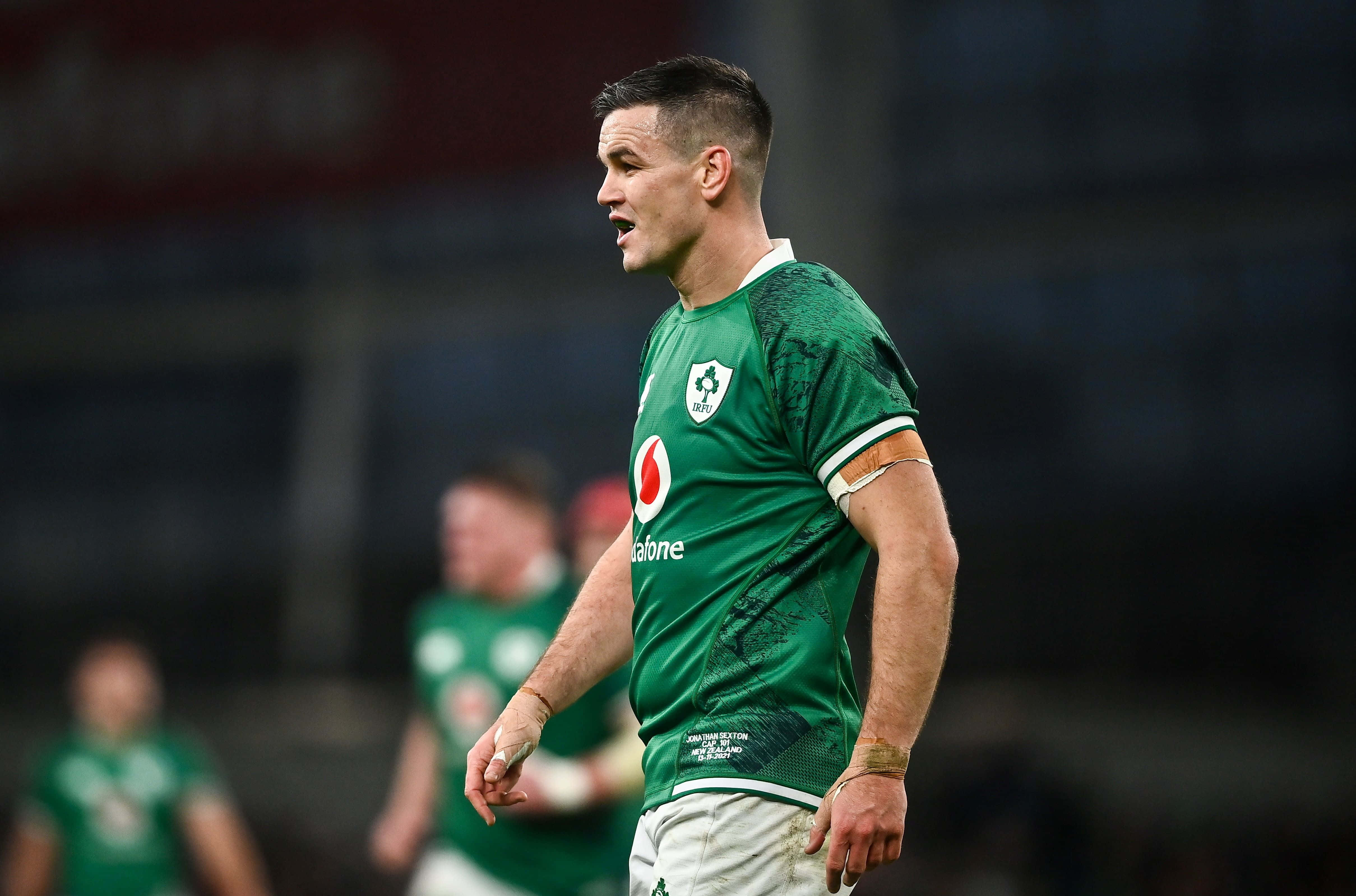 Ireland Rugby 桌布 壁紙 — 一名專注的欖球運動員身穿帶有三葉草標誌的綠色球衣，在球場燈光下進行比賽時站在場上。