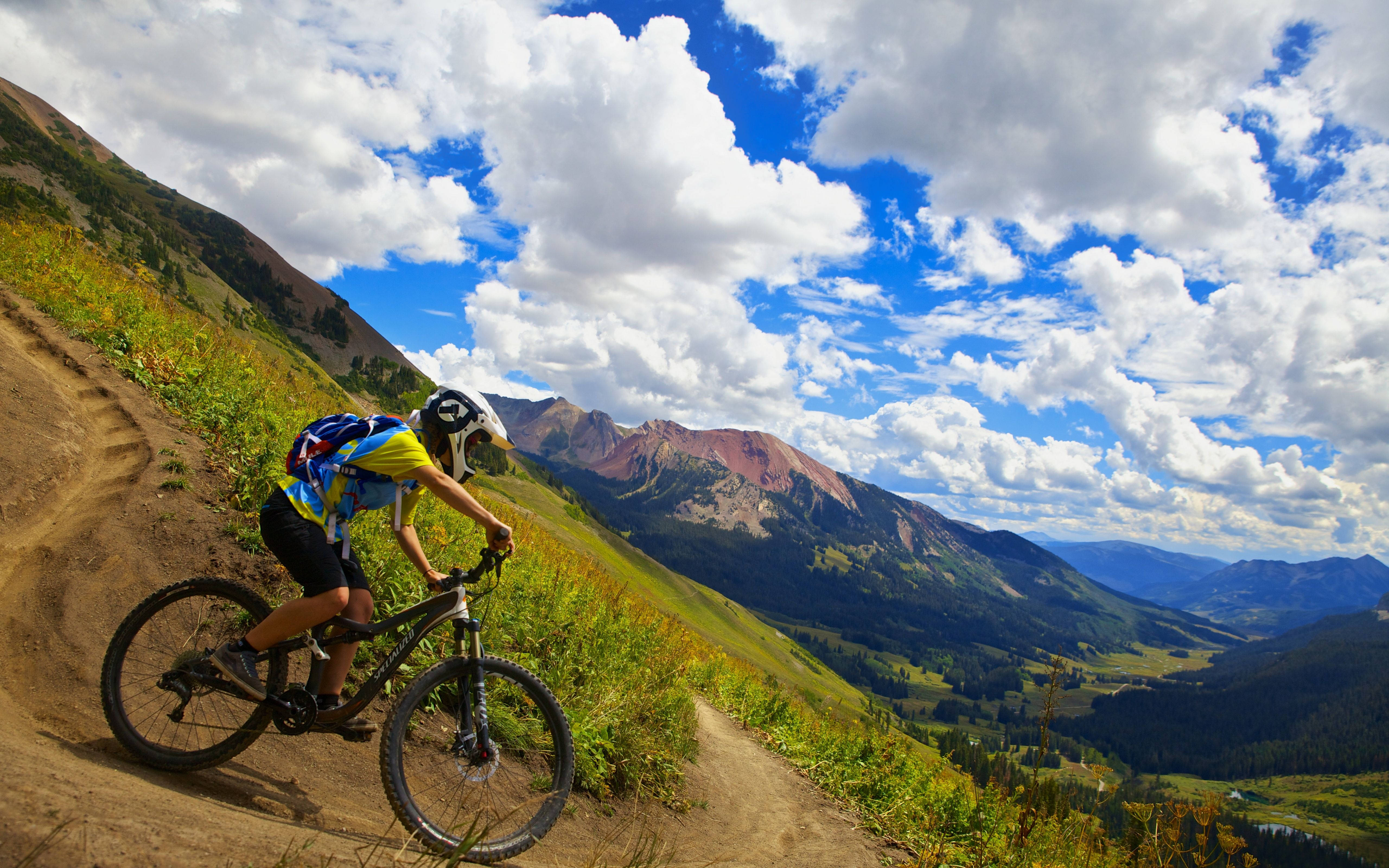 Mountain Bike 桌布 壁紙 — 一名山地單車手在泥徑上傾身過彎，背景是戲劇性的雲層和崎嶇的山峰。