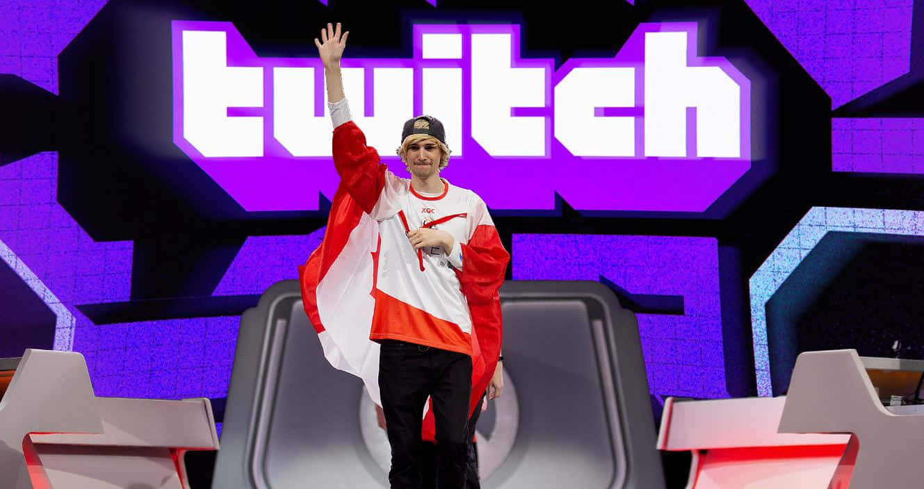 Minecraft Twitch Streamers 桌布 壁紙 — 一名年輕男子在掛有加拿大國旗的Twitch舞台上自豪地揮手，身穿紅白球衣。