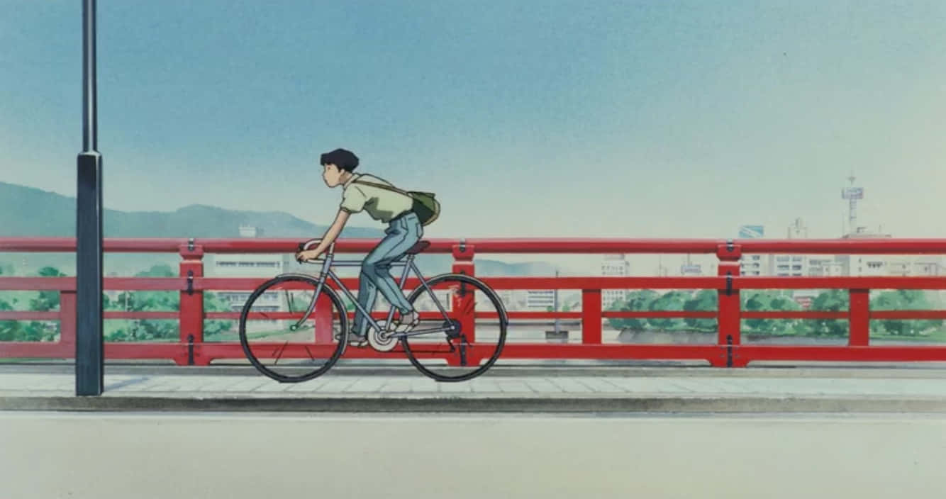 Studio Ghibli Ocean Waves 桌布 壁紙 — 一名年輕男子在晴朗的藍天下，騎著單車穿過一座鮮紅色的橋，遠處有山脈和城市景觀。