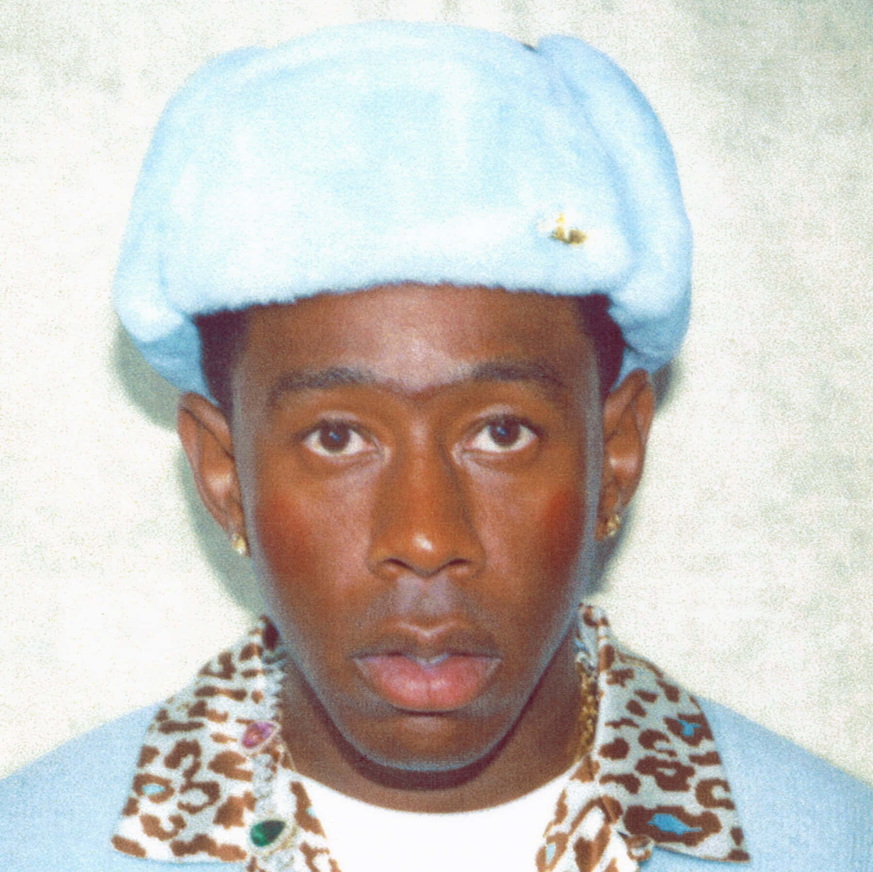 tyler the creator 桌布 壁紙 — 一名年輕男子戴著淺藍色絨毛貝雷帽，穿著飾有彩色寶石的豹紋領，背景為純色。