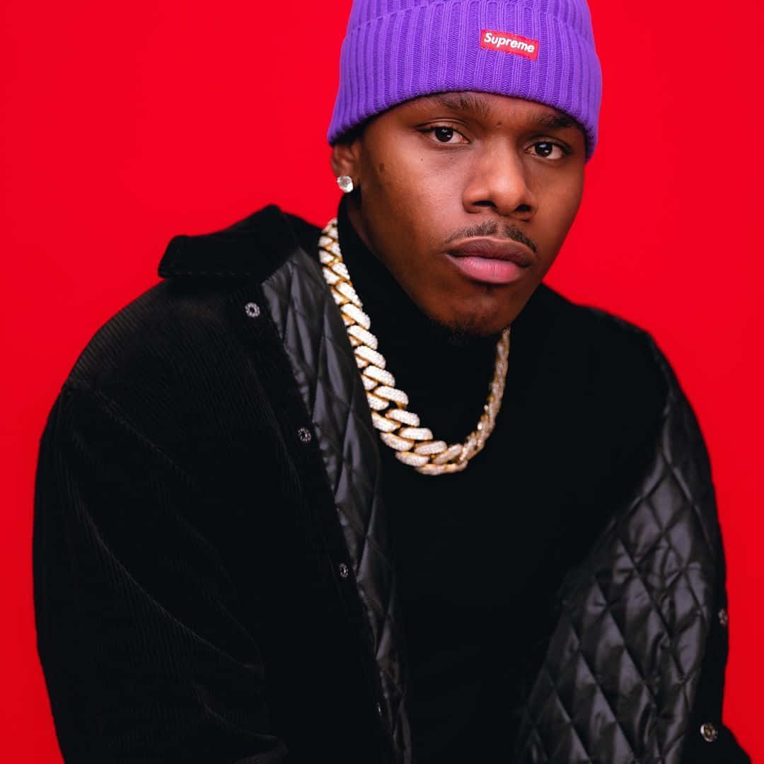 Dababy 桌布 壁紙 — 一名年輕男子戴著紫色Supreme冷帽和金鏈，在鮮紅色背景下強烈凝視。