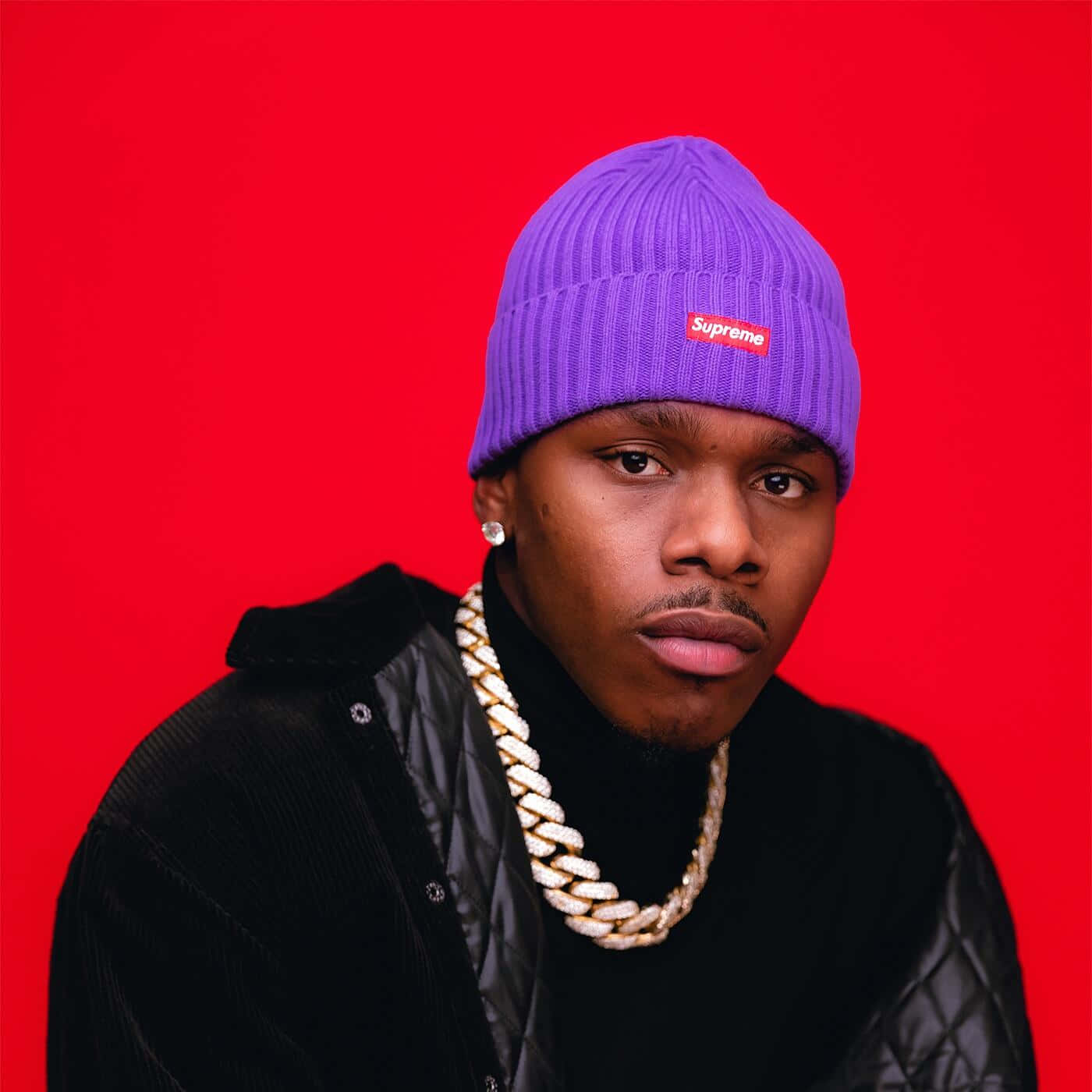 Dababy 桌布 壁紙 — 一名年輕男子戴著紫色Supreme冷帽和金鏈，在鮮豔的紅色背景前凝視。