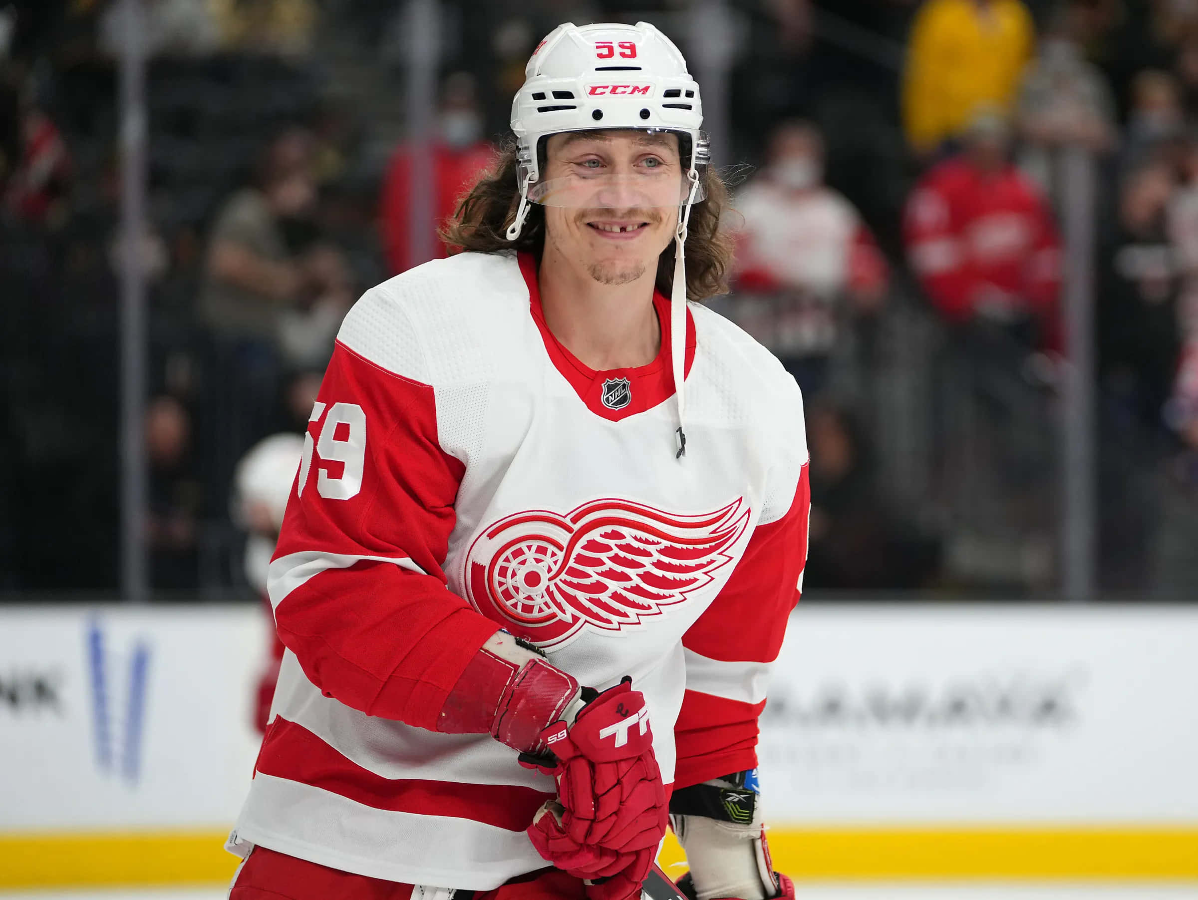 Tyler Bertuzzi 桌布 壁紙 — 一名微笑的曲棍球運動員身穿紅白相間的底特律紅翼隊39號球衣，在比賽期間站在冰上。