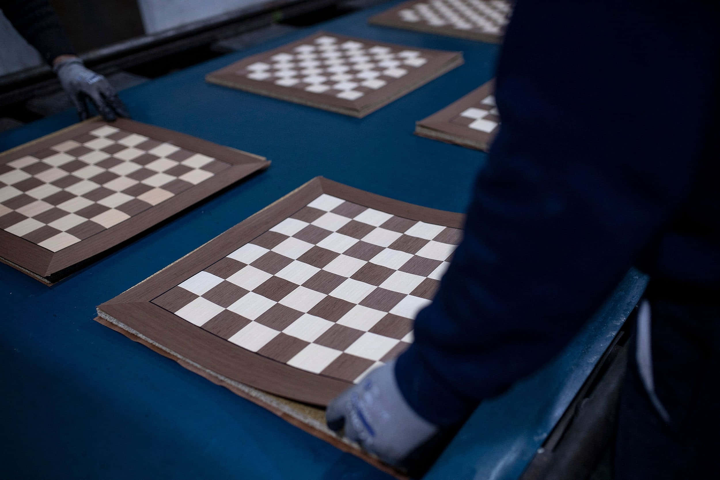 Chessboard 桌布 壁紙 — 一名戴手套的工人在工廠環境中的藍色傳送帶上組裝木製棋盤。