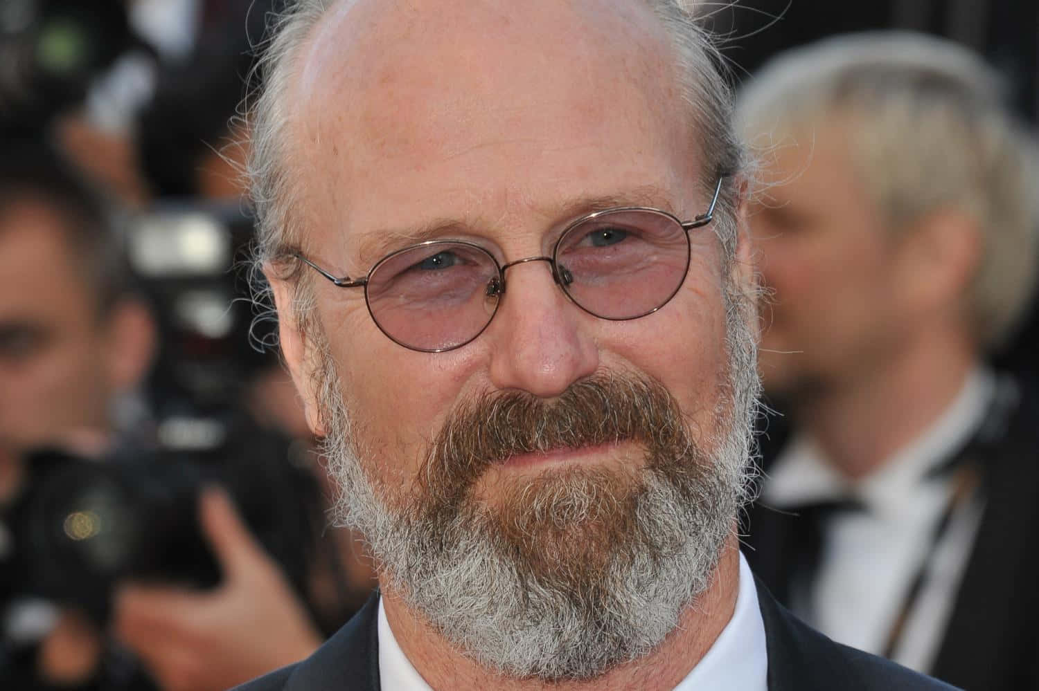 William Hurt 桌布 壁紙 — 一名戴眼鏡、留灰白鬍鬚的男子在紅地毯活動上的特寫，背景有攝影師。