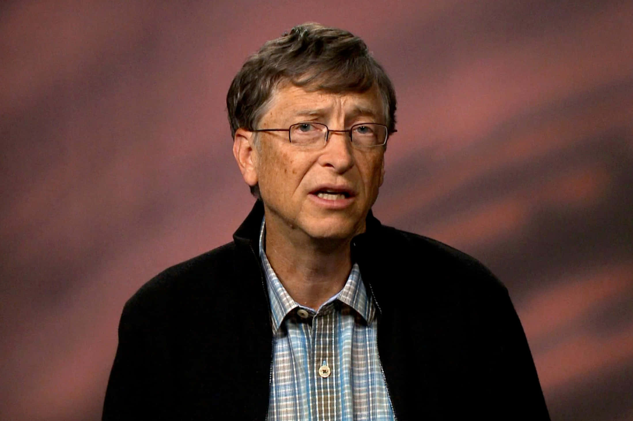 Bill Gates 桌布 壁紙 — 一名戴眼鏡、身穿格仔恤衫嘅男人喺模糊嘅偏紅背景前講嘢。