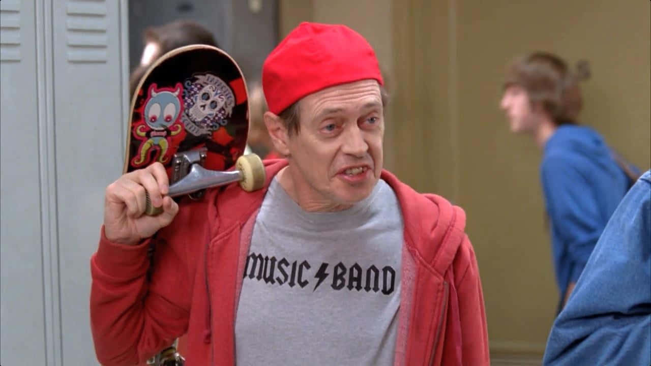 steve buscemi 桌布 壁紙 — 一名戴紅色冷帽、穿連帽衛衣的男子站在學校走廊，手持一塊帶有卡通圖案的滑板。