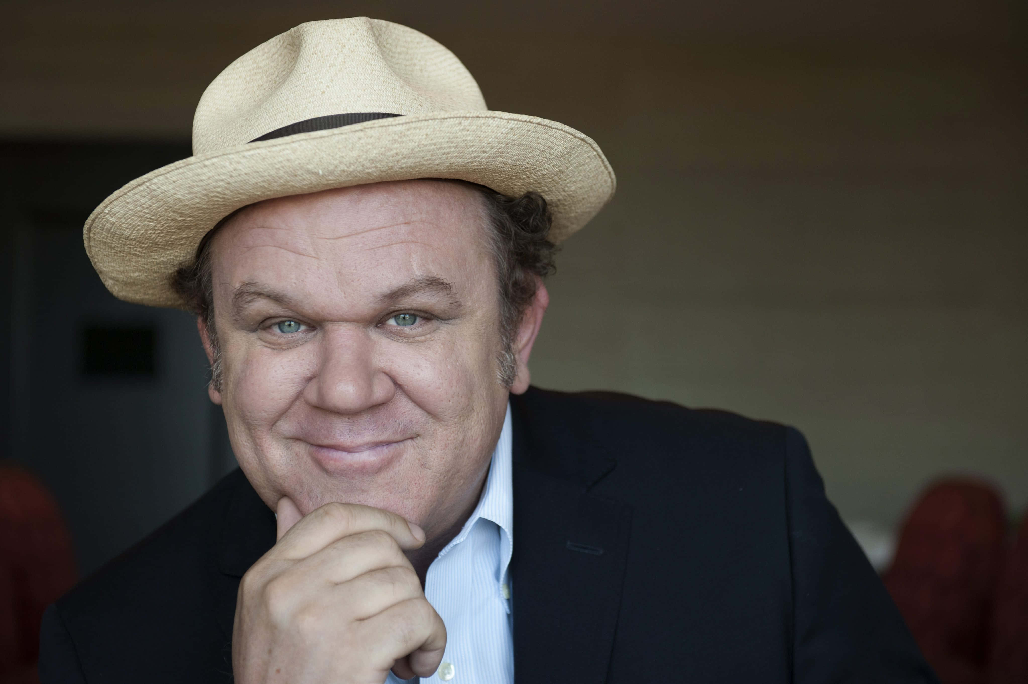 John C. Reilly 桌布 壁紙 — 一名戴草帽穿西裝的男子在室內手托下巴，若有所思地微笑。