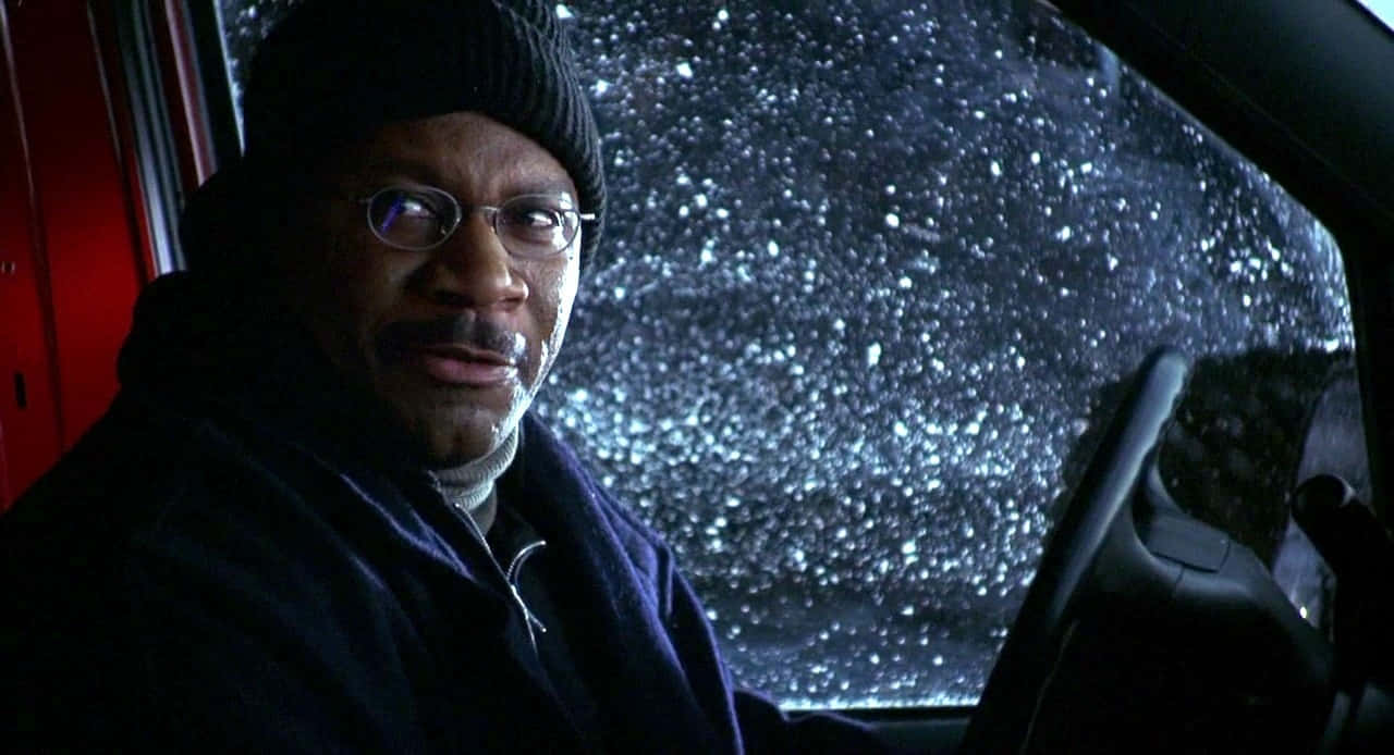 Ving Rhames 桌布 壁紙 — 一名戴著冷帽和眼鏡的男子在車內凝視前方，雪花在夜間劃過擋風玻璃。