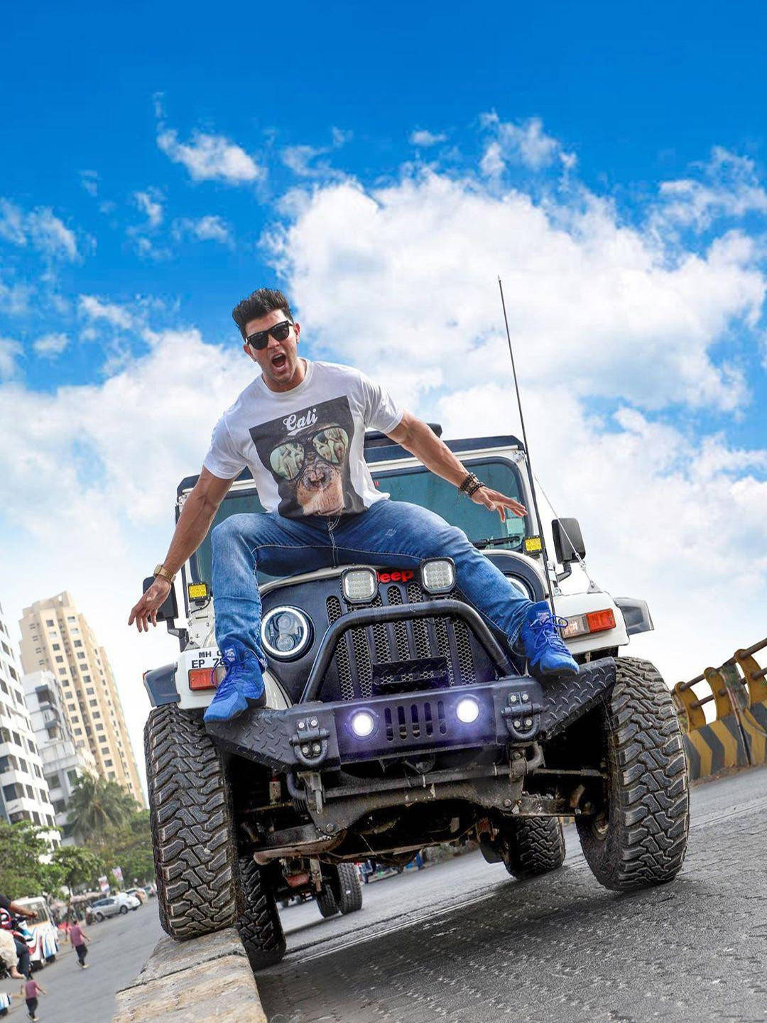 Jeep 動圖 桌布 壁紙 — 一名戴著太陽眼鏡和牛仔褲的男子坐在一輛升高了的白色Jeep上，車頭燈發光，背景是晴朗的藍天和蓬鬆的白雲。