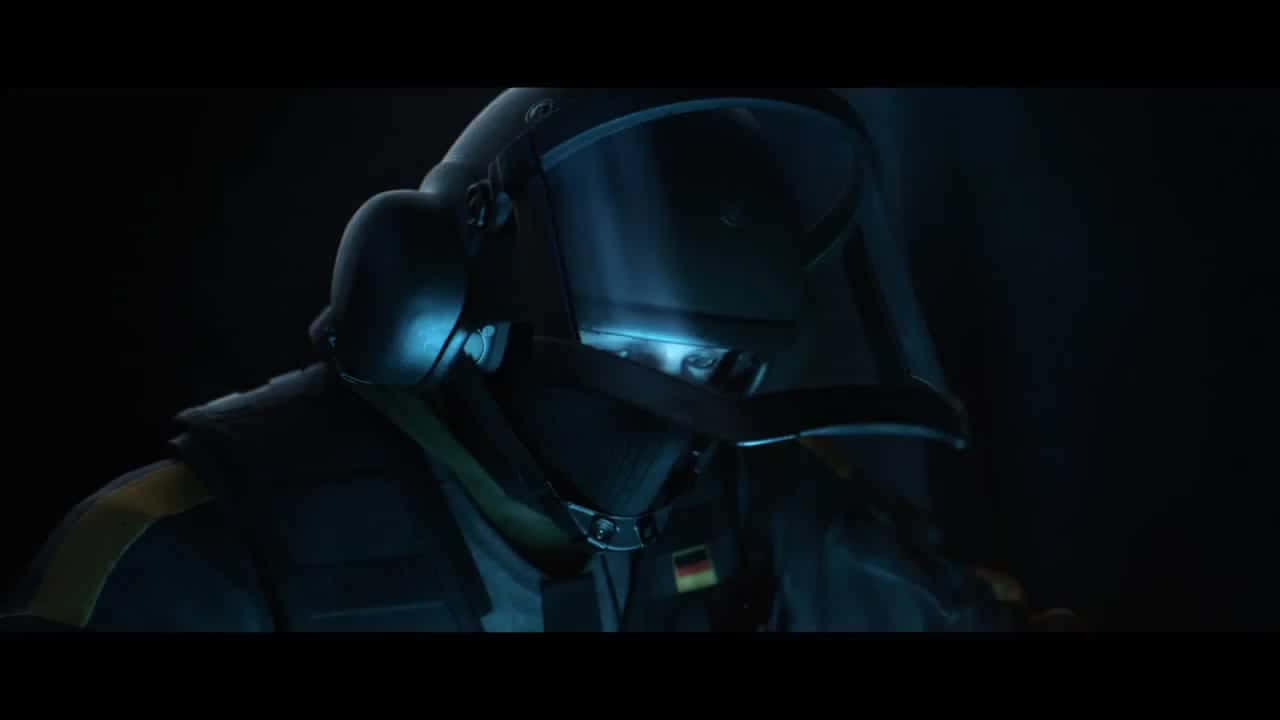 Rainbow Six Siege Bandit 桌布 壁紙 — 一名戴著深色頭盔、帶有發光藍色面罩的士兵站在陰暗的黑暗中，可見德國國旗臂章。
