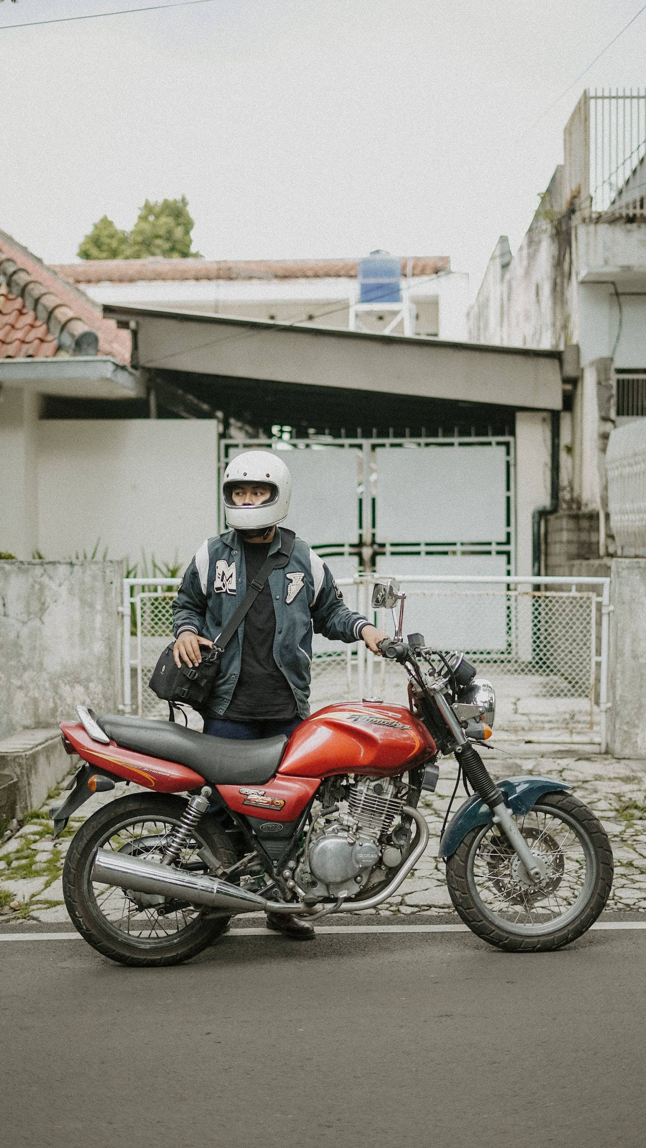 bike riding 桌布 壁紙 — 一名戴著白色頭盔的人站在一輛停放在寧靜住宅街道上的紅藍色電單車旁。