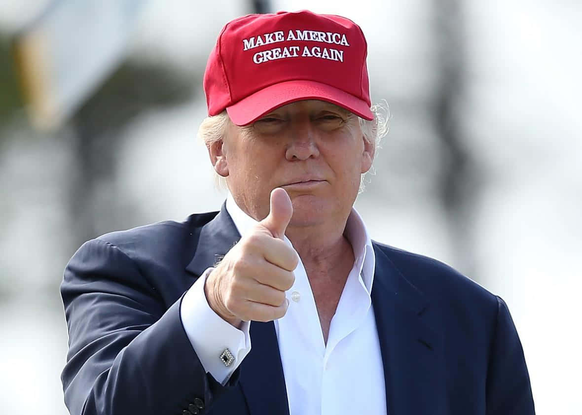trump 桌布 壁紙 — 一名戴著紅色MAGA帽子的男士，身穿深色西裝和白襯衫，豎起大拇指。
