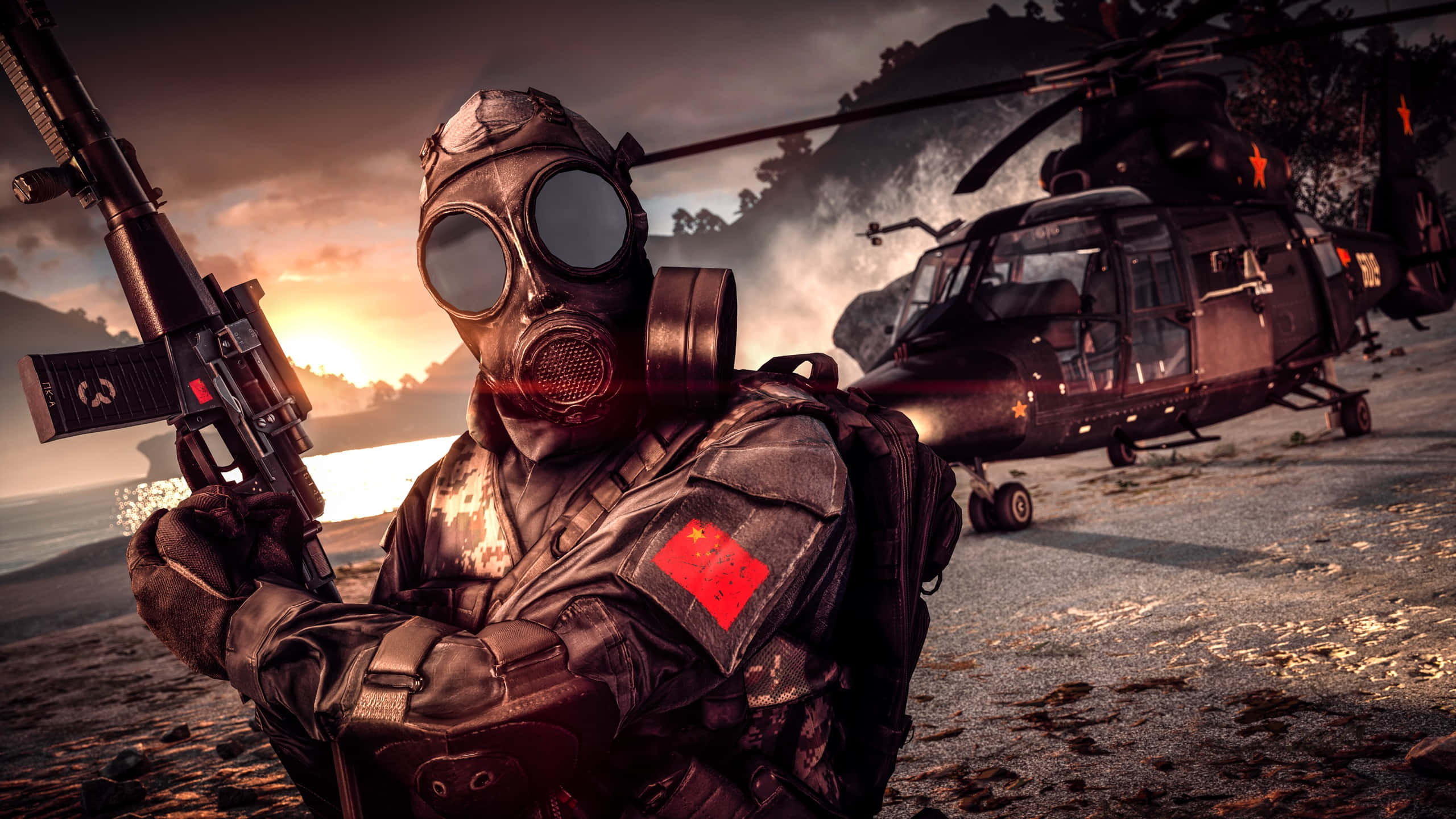 Battlefield Vehicles 桌布 壁紙 — 一名戴著防毒面具和戰術裝備的士兵在日落時分的沙灘上持步槍，附近有一架軍用直升機。