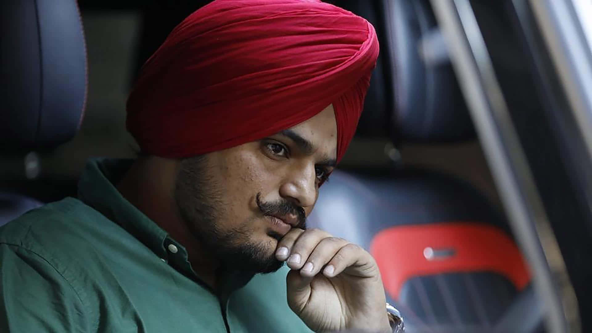 Sidhu Moose Wala 桌布 壁紙 — 一名戴著鮮紅色頭巾的男子坐在車內沉思，手放在嘴邊，專注地向前凝視。