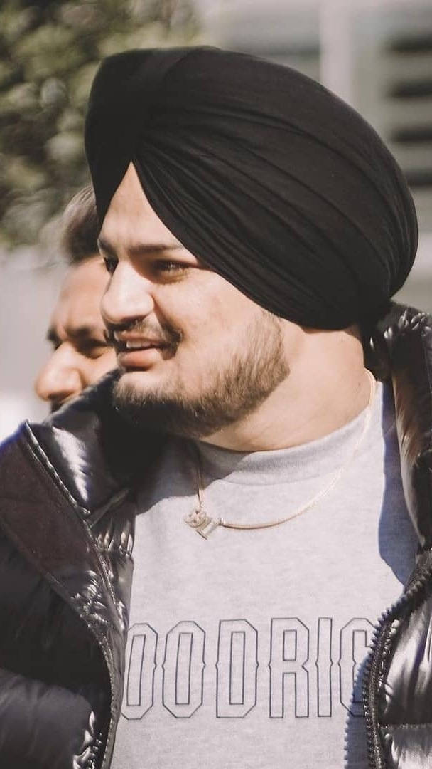 Indian 桌布 壁紙 — 一名戴著黑色頭巾和羽絨外套的男子在明亮的陽光下溫暖地微笑。