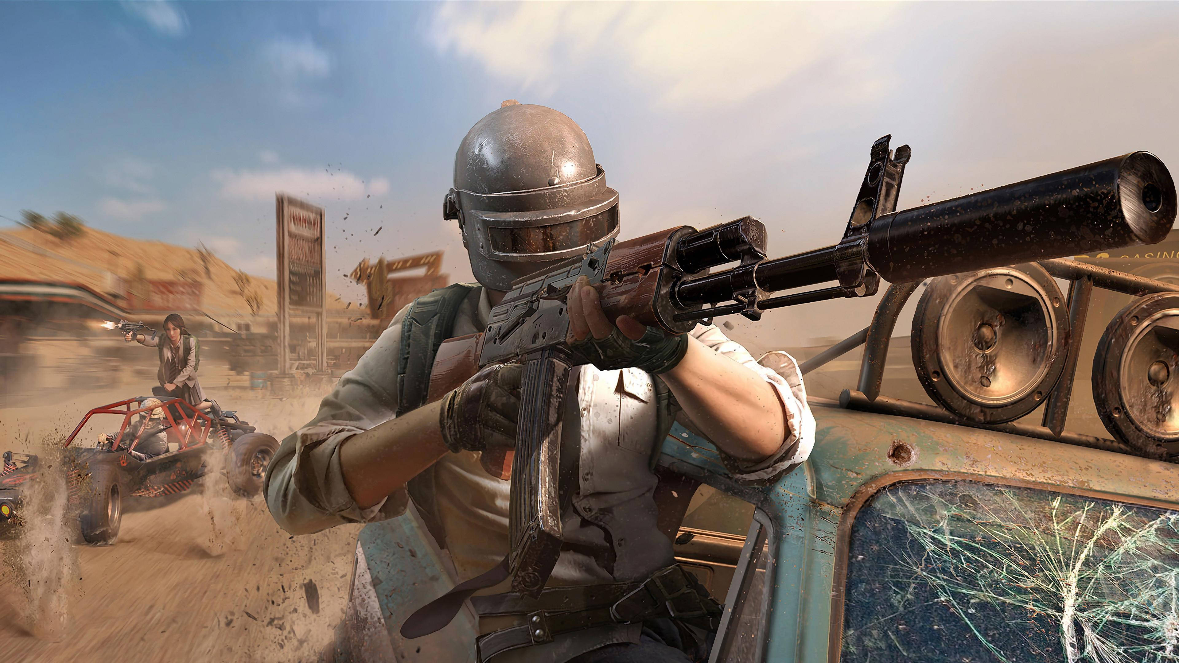 pubg 4K gaming 桌布 壁紙 — 一名戴頭盔的士兵從一輛損壞的藍色車輛上瞄準步槍，而另一名玩家在塵土飛揚的沙漠戰場上駕駛沙灘車。