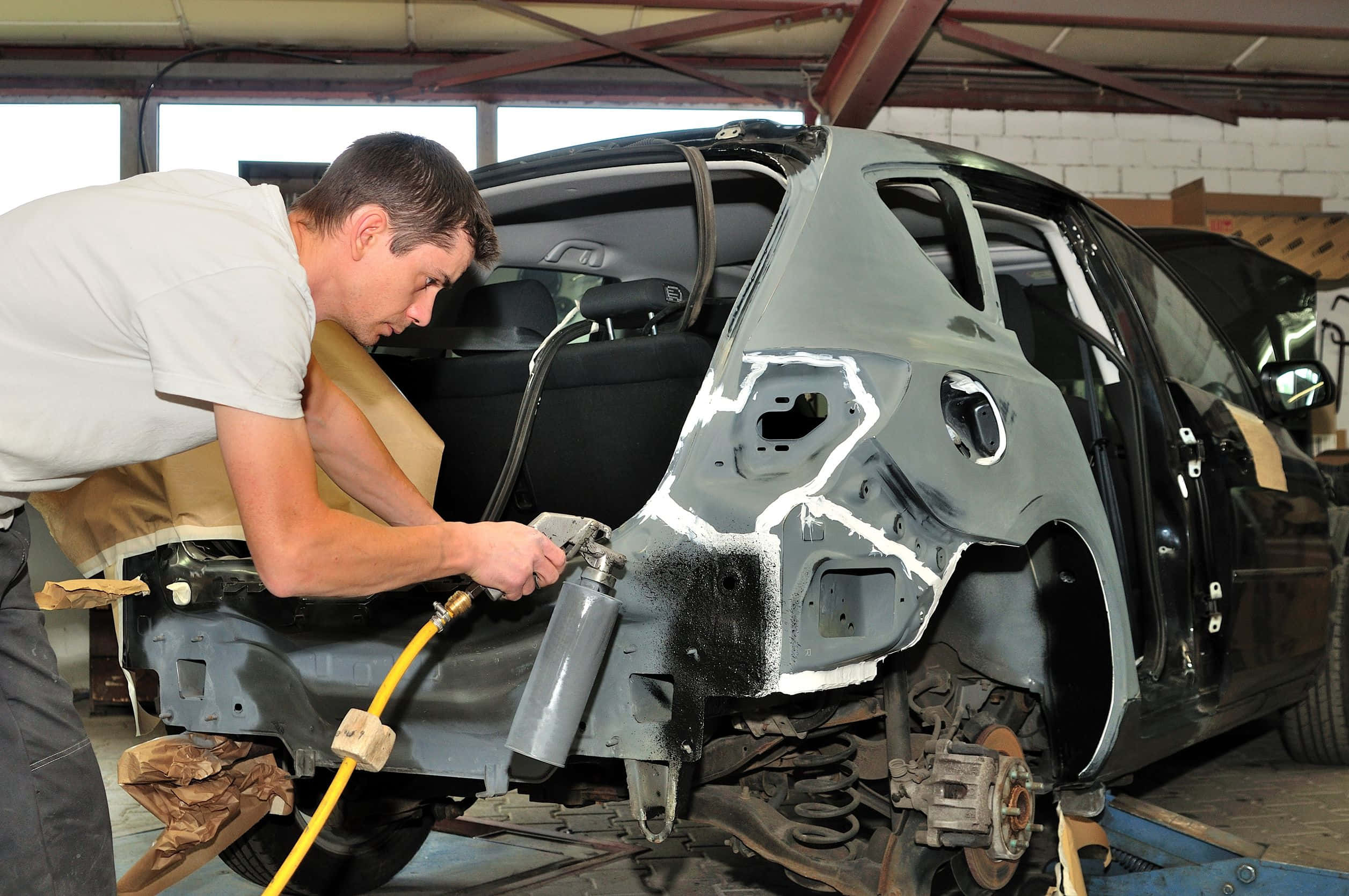 Car Repair 桌布 壁紙 — 一名技師在光線充足的車庫中，小心地將底漆噴灑在正在進行車身修理的汽車裸露金屬框架上。