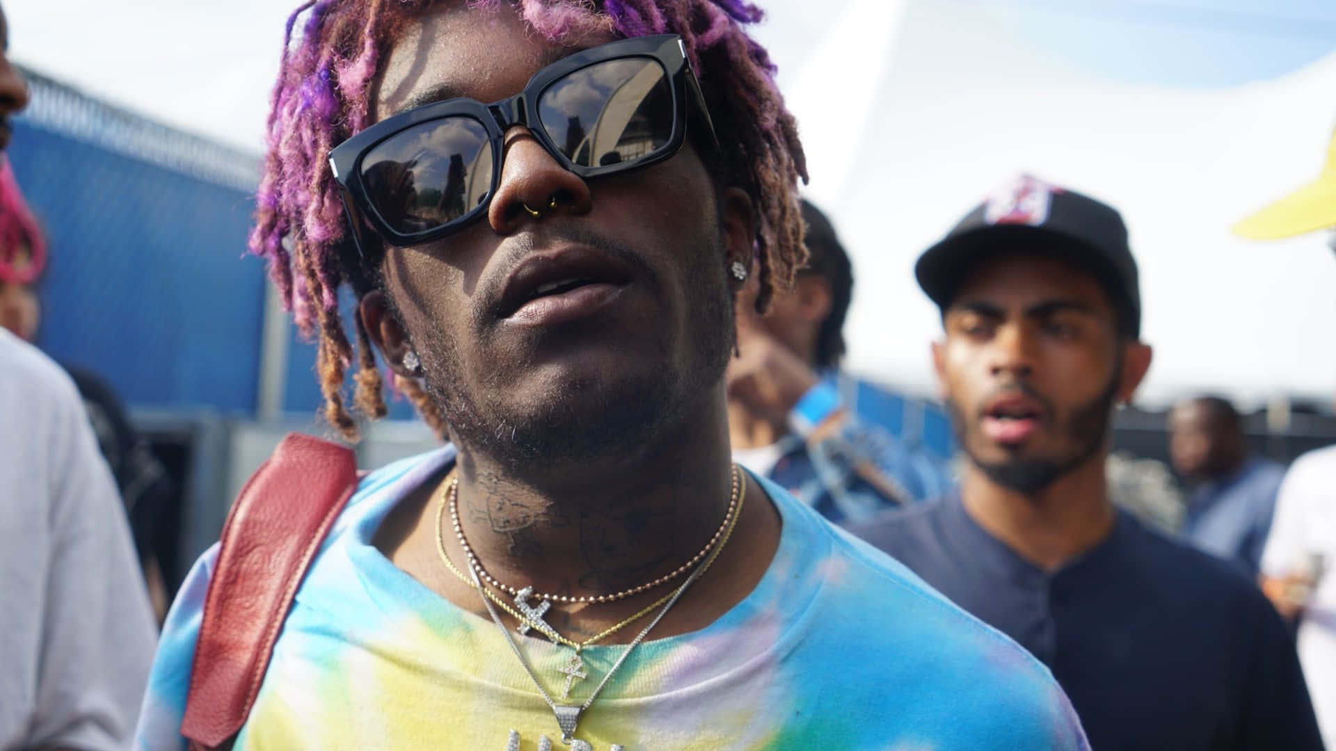 Lil Uzi Vert 桌布 壁紙 — 一名擁有充滿活力的紫色和棕色辮子、戴著大黑色太陽眼鏡的男子，穿著紮染襯衫和層疊項鍊，向上仰望。