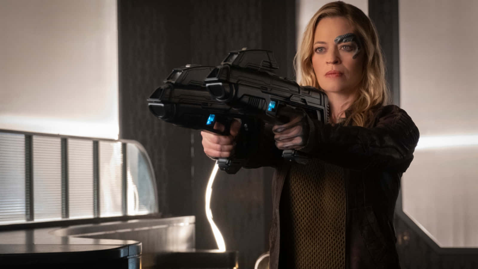 Jeri Ryan 桌布 壁紙 — 一名擁有電子眼植入物的女性在時尚的科幻室內環境中瞄準一把未來風格的發光爆能槍。
