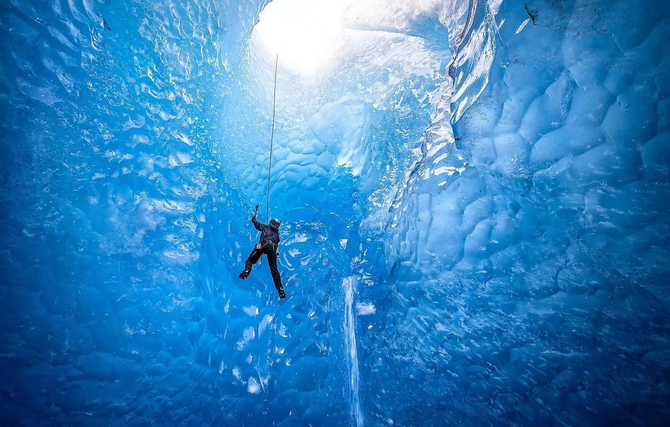 Ice Climbing 桌布 壁紙 — 一名攀岩者正下降至一個發光的藍色冰洞，陽光穿透上方的冰層天花板。
