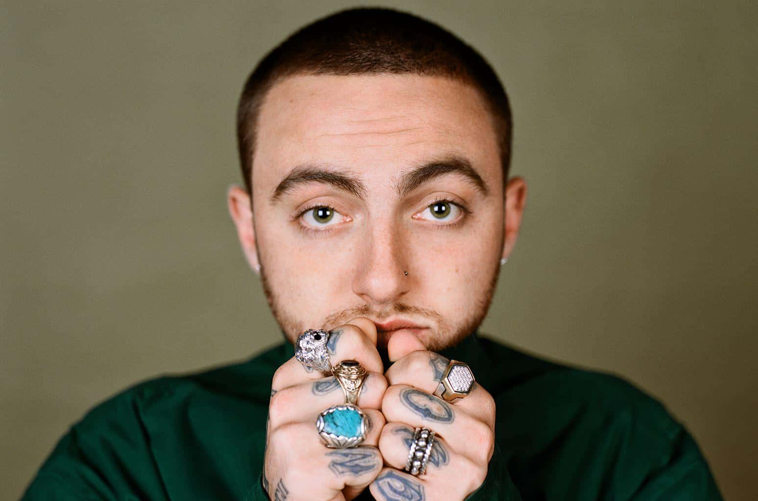 Mac Miller 桌布 壁紙 — 一名有紋身及戴多枚戒指的男子，在柔和的綠色背景下凝視鏡頭。