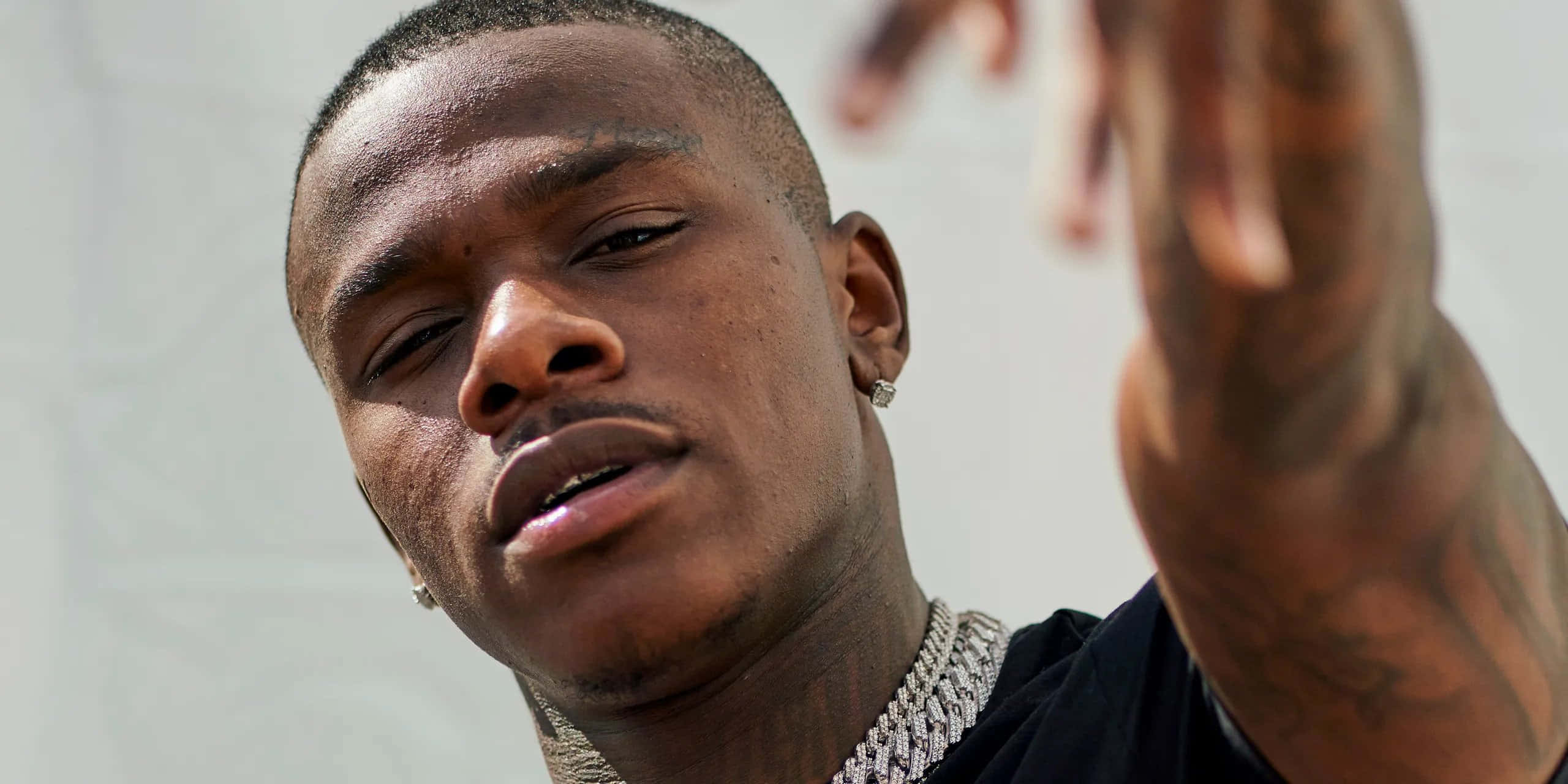 Dababy 桌布 壁紙 — 一名有紋身和鑽石鏈的男子舉起一隻手，近距離凝視鏡頭。