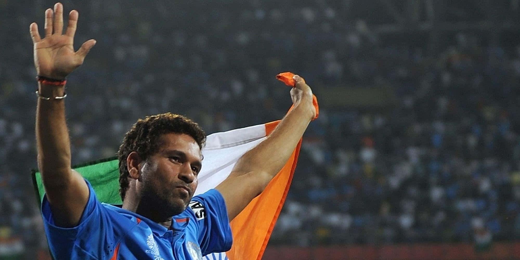Sachin Tendulkar 桌布 壁紙 — 一名板球運動員在夜間體育館向歡呼的人群揮舞印度國旗並舉手。