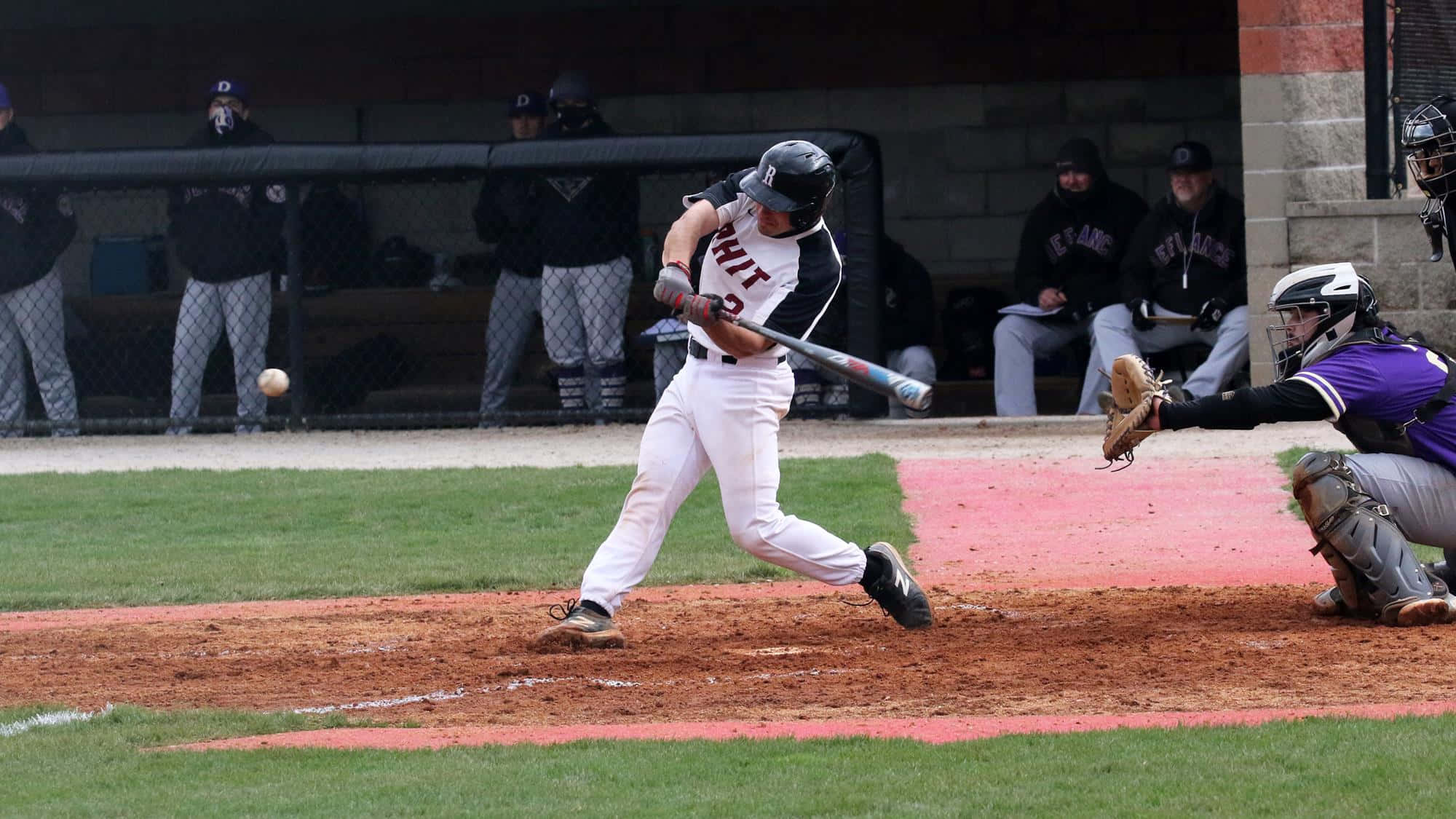College Baseball 桌布 壁紙 — 一名棒球手揮棒擊球，捕手蹲在本壘板後方準備接球。
