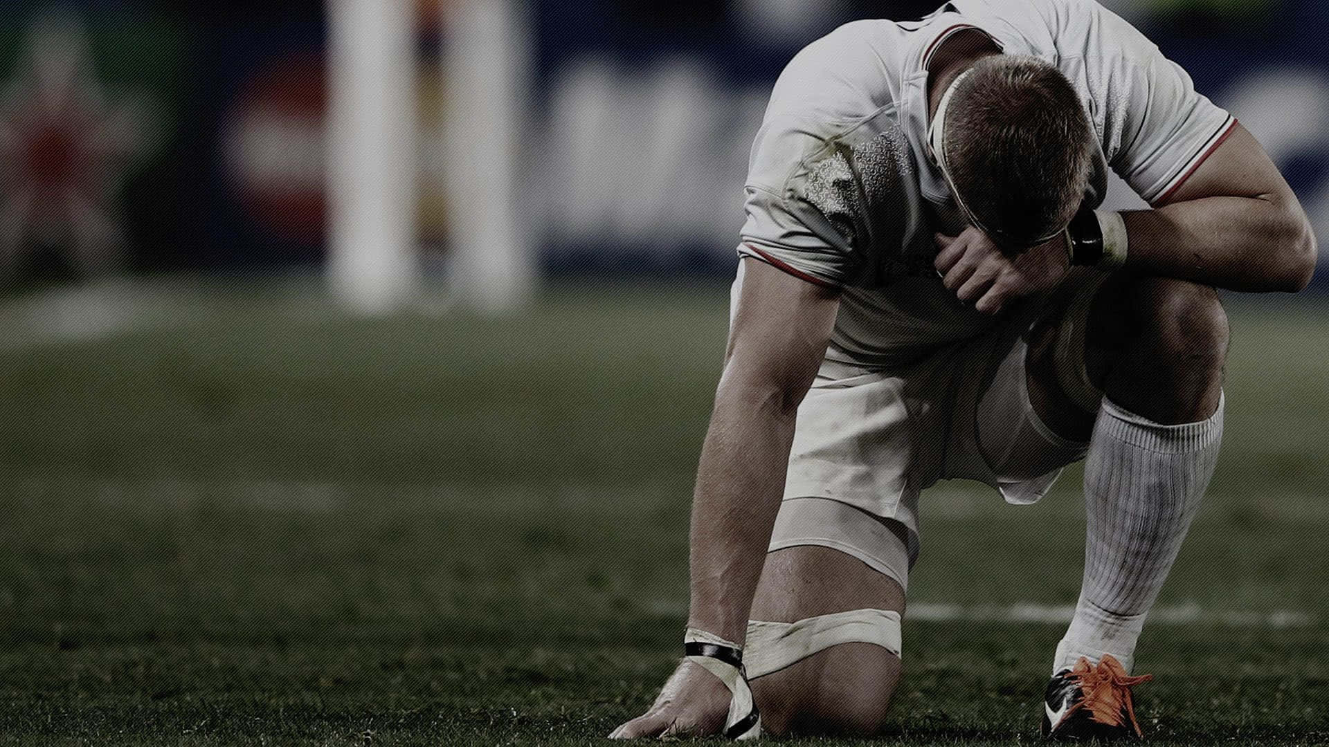 Rugby 桌布 壁紙 — 一名欖球球員在球場燈光下輸波後跪在草地上雙手抱頭。