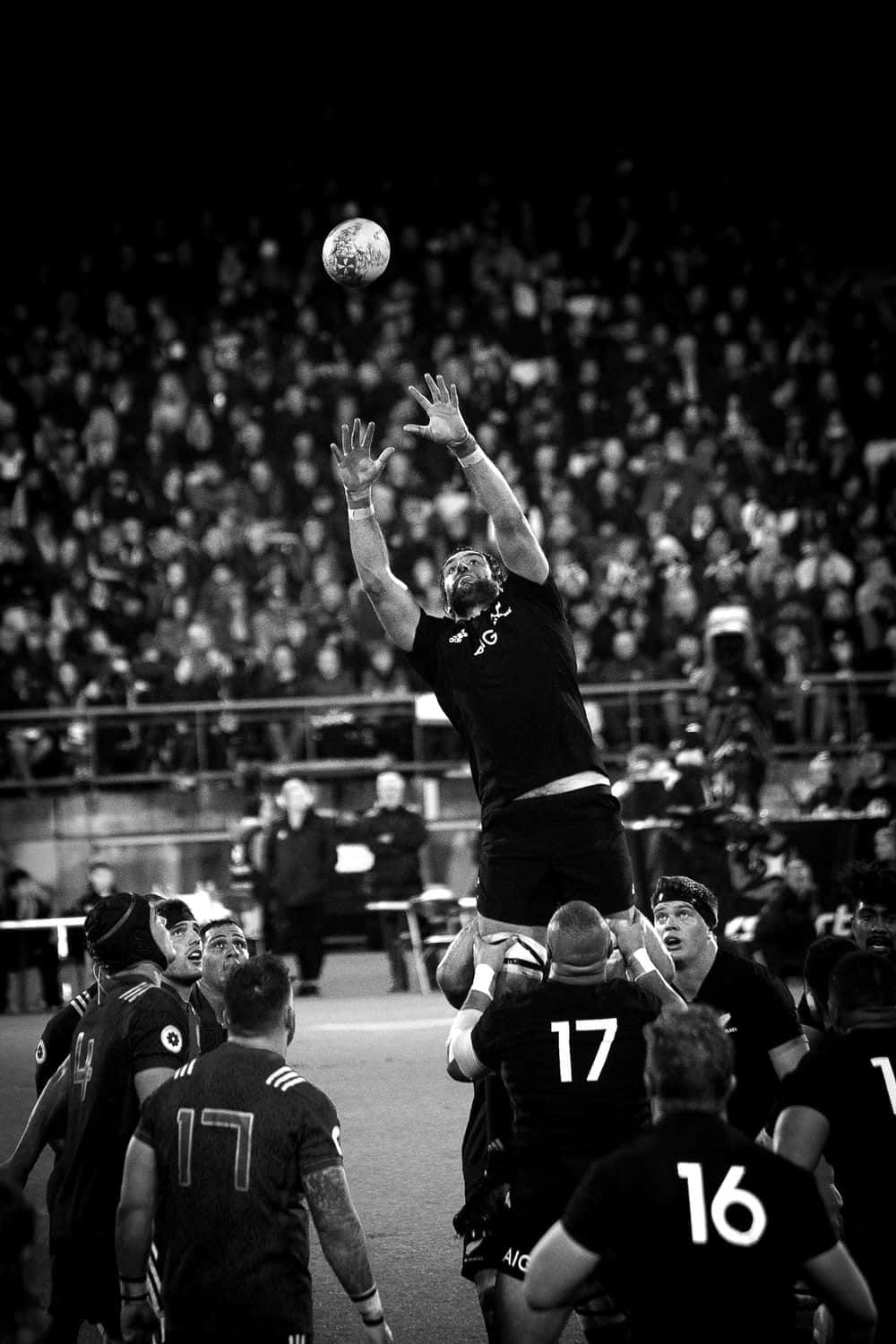 Rugby 桌布 壁紙 — 一名欖球運動員在球場燈光下於界外球中高高躍起接球，黑白畫面。