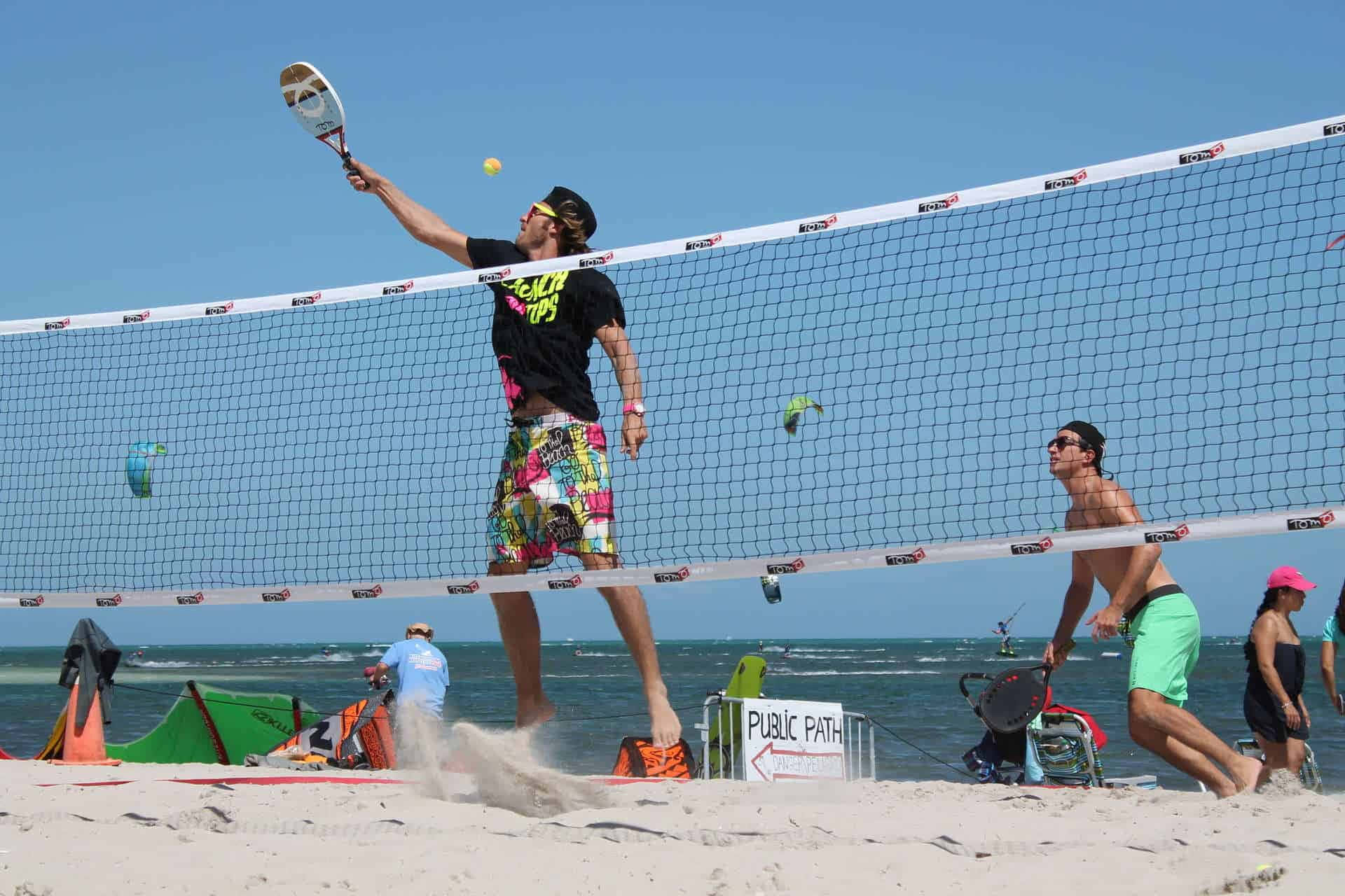 Beach Tennis 桌布 壁紙 — 一名沙灘排球運動員在陽光明媚的日子跳起扣球，身後海浪拍打。