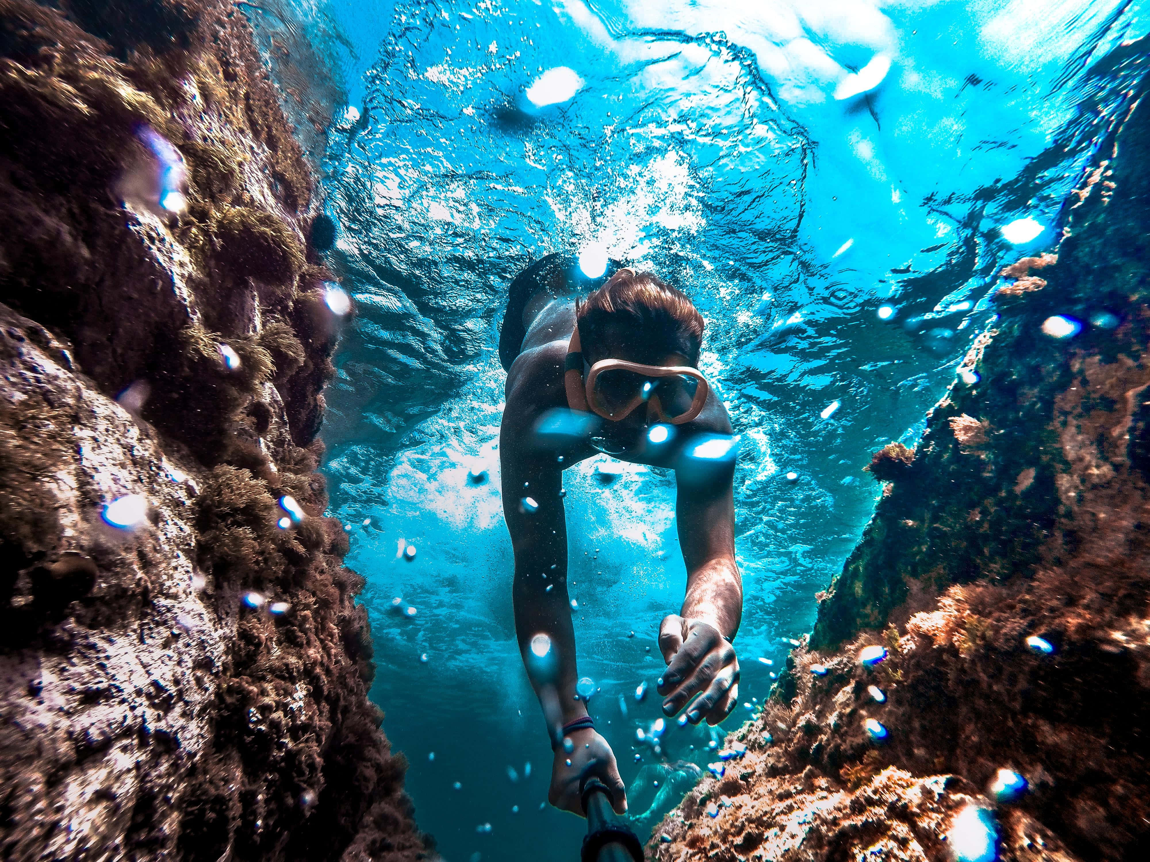 diving 桌布 壁紙 — 一名浮潛者游過陽光照耀的水下峽谷，四周環繞著岩壁和閃爍的藍色海水。