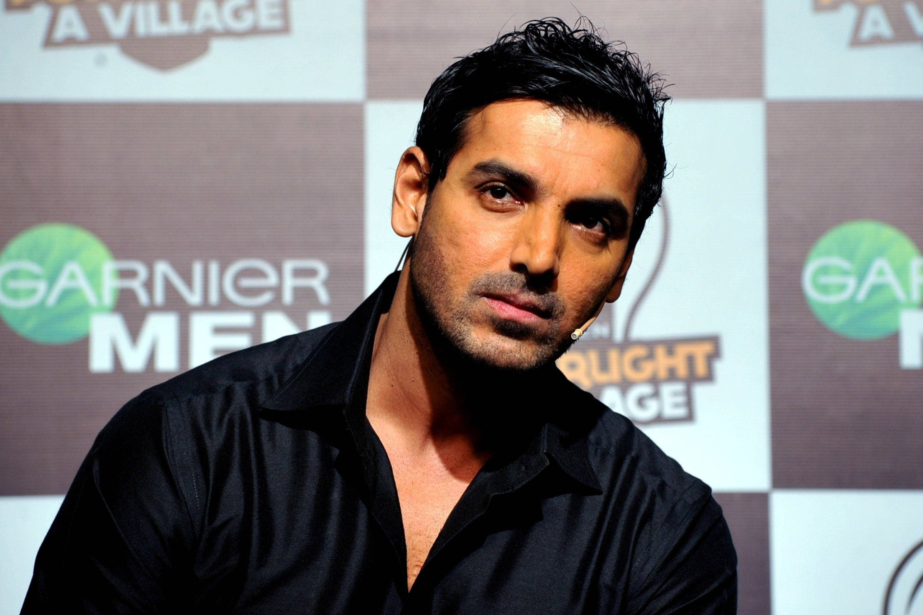 Bollywood HD 桌布 壁紙 — 一名深色頭髮、留有鬍渣的男子，身穿黑色襯衫，背景為帶有Garnier Men標誌的格紋圖案。