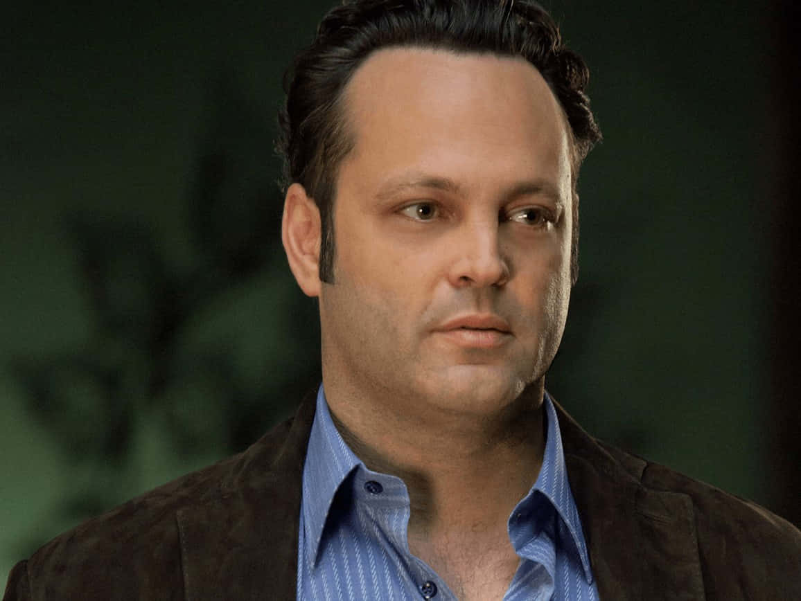 Vince Vaughn 桌布 壁紙 — 一名深色頭髮、表情嚴肅的男子，在模糊的綠色背景前，穿著藍色襯衫外搭棕色外套。