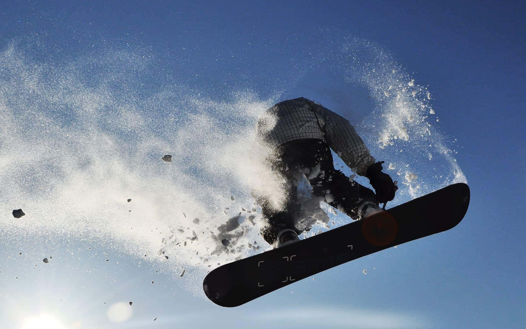 Winter Sports 桌布 壁紙 — 一名滑雪板運動員在清澈的藍天下高高躍起，將雪粒戲劇性地噴灑到空中。