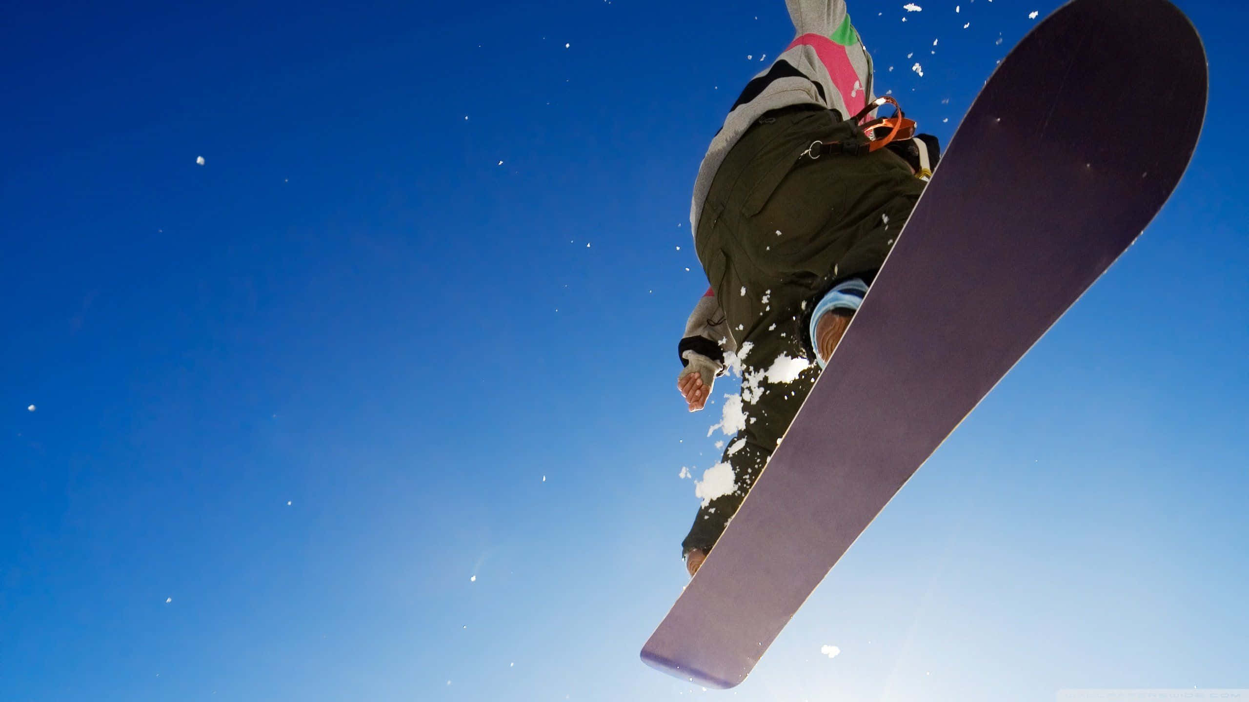 Winter Sports 桌布 壁紙 — 一名滑雪板運動員在清澈的藍天中翱翔，雪從滑板上飛濺而出。