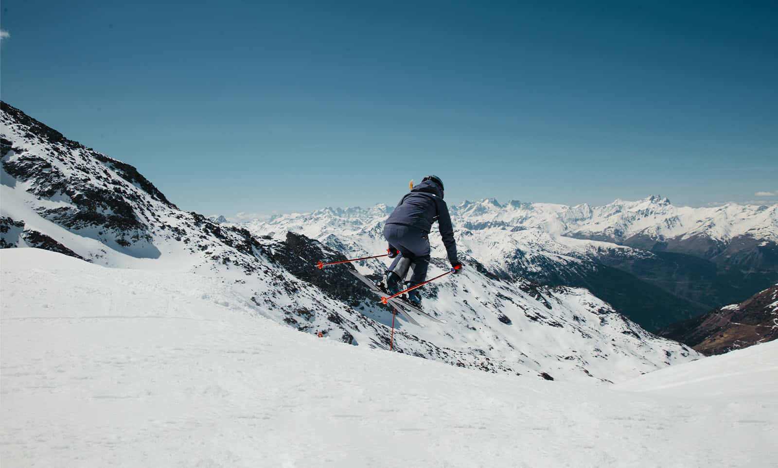 Skiing 桌布 壁紙 — 一名滑雪者在晴朗的藍天下，於廣闊的雪景之上，飛翔在清爽的山間空氣中。