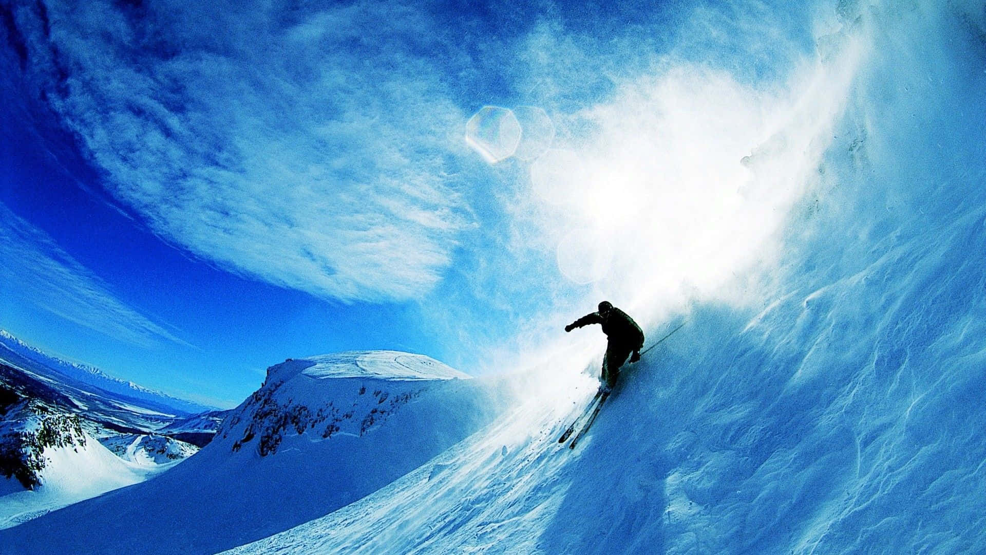 Winter Sports 桌布 壁紙 — 一名滑雪者在陡峭的山坡上劃過粉雪，天空湛藍，雲朵輕柔。