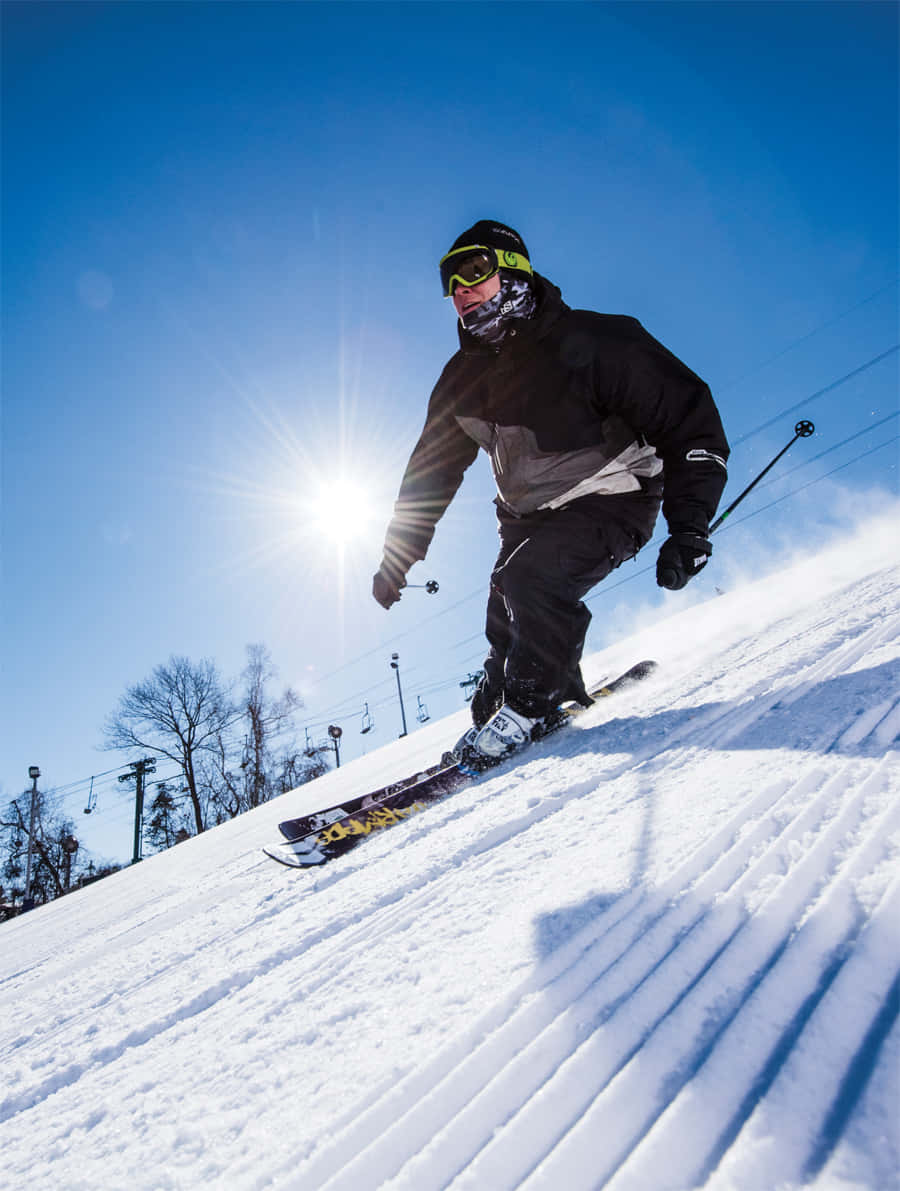 Skiing 桌布 壁紙 — 一名滑雪者在陽光照耀的雪坡上刻滑而下，背景有滑雪纜車和光禿禿的樹木，天空清澈湛藍。